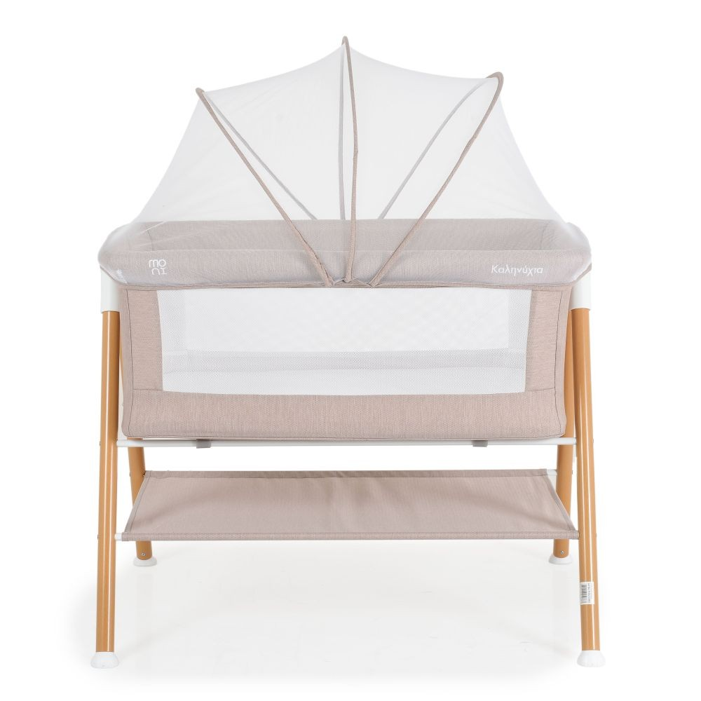 Cuna beige para bebés con mosquitera. Patas de madera y un estante de almacenamiento. Fondo blanco.