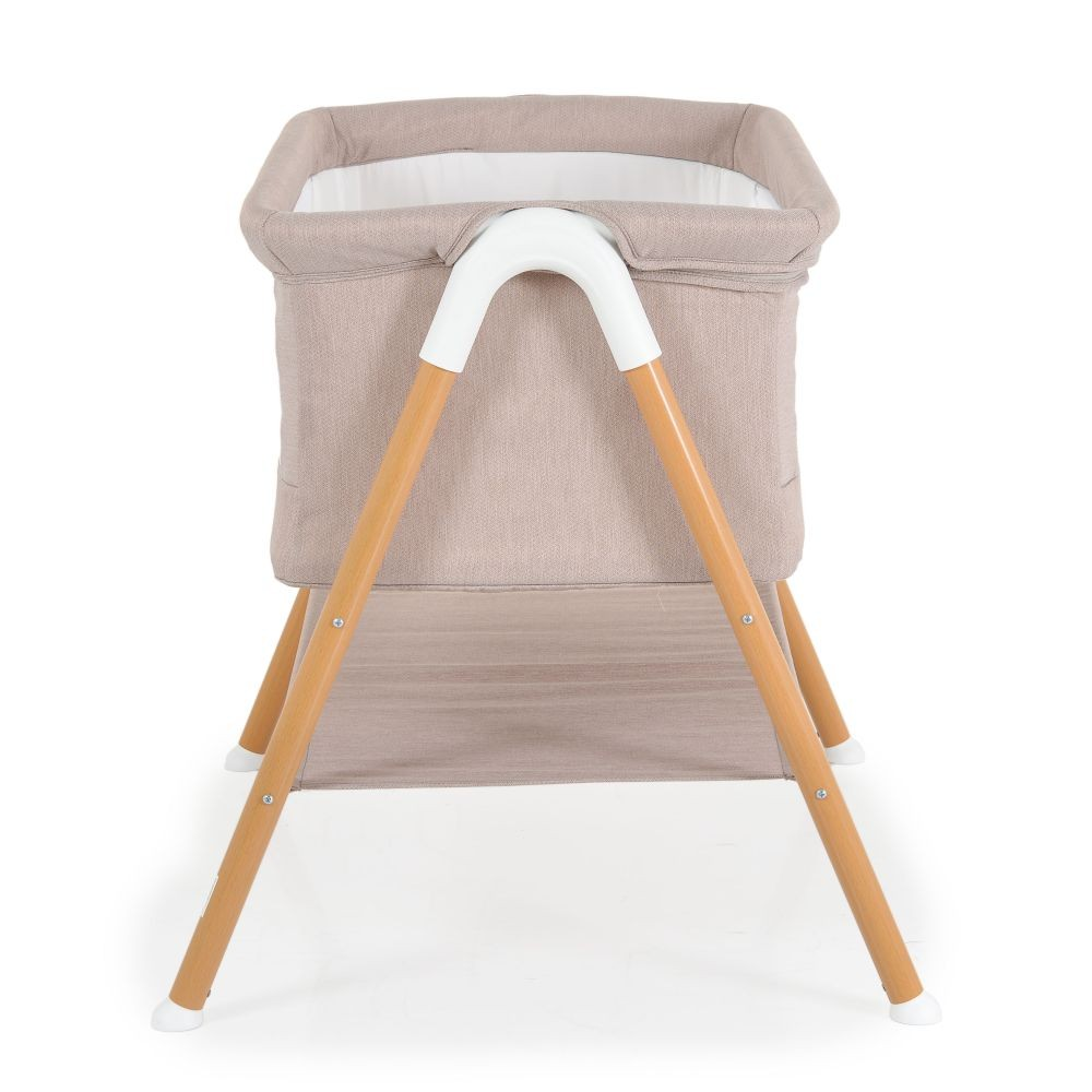 Cuna beige para bebé con patas de madera. Fondo blanco. Vista frontal.