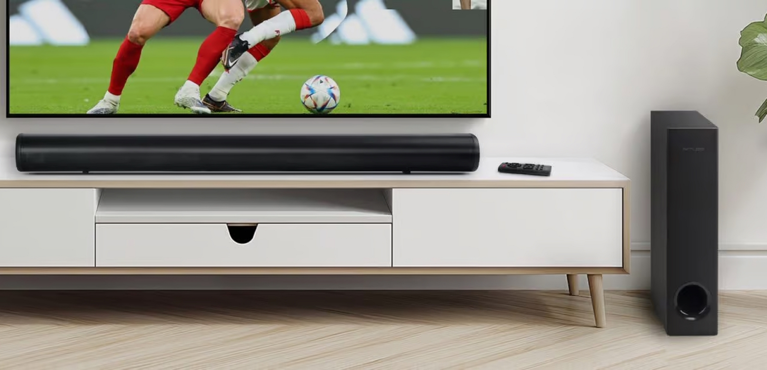 Soundbar nera su mobile bianco sotto TV, con partita di calcio.