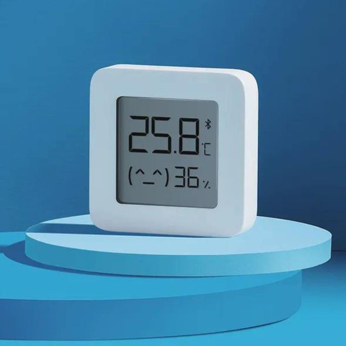 Pantalla digital cuadrada blanca que muestra temperatura y humedad, sobre un pedestal azul.