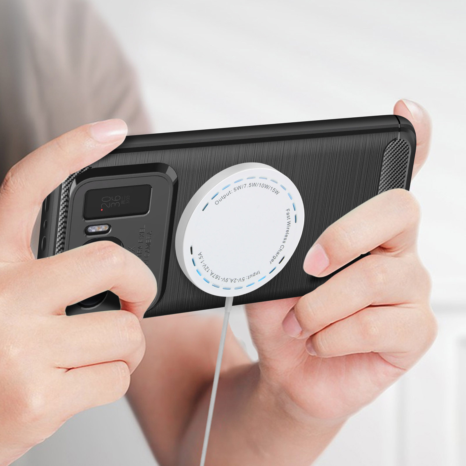 Una persona tiene in mano un telefono nero con un caricatore wireless. Il telefono ha una fotocamera.