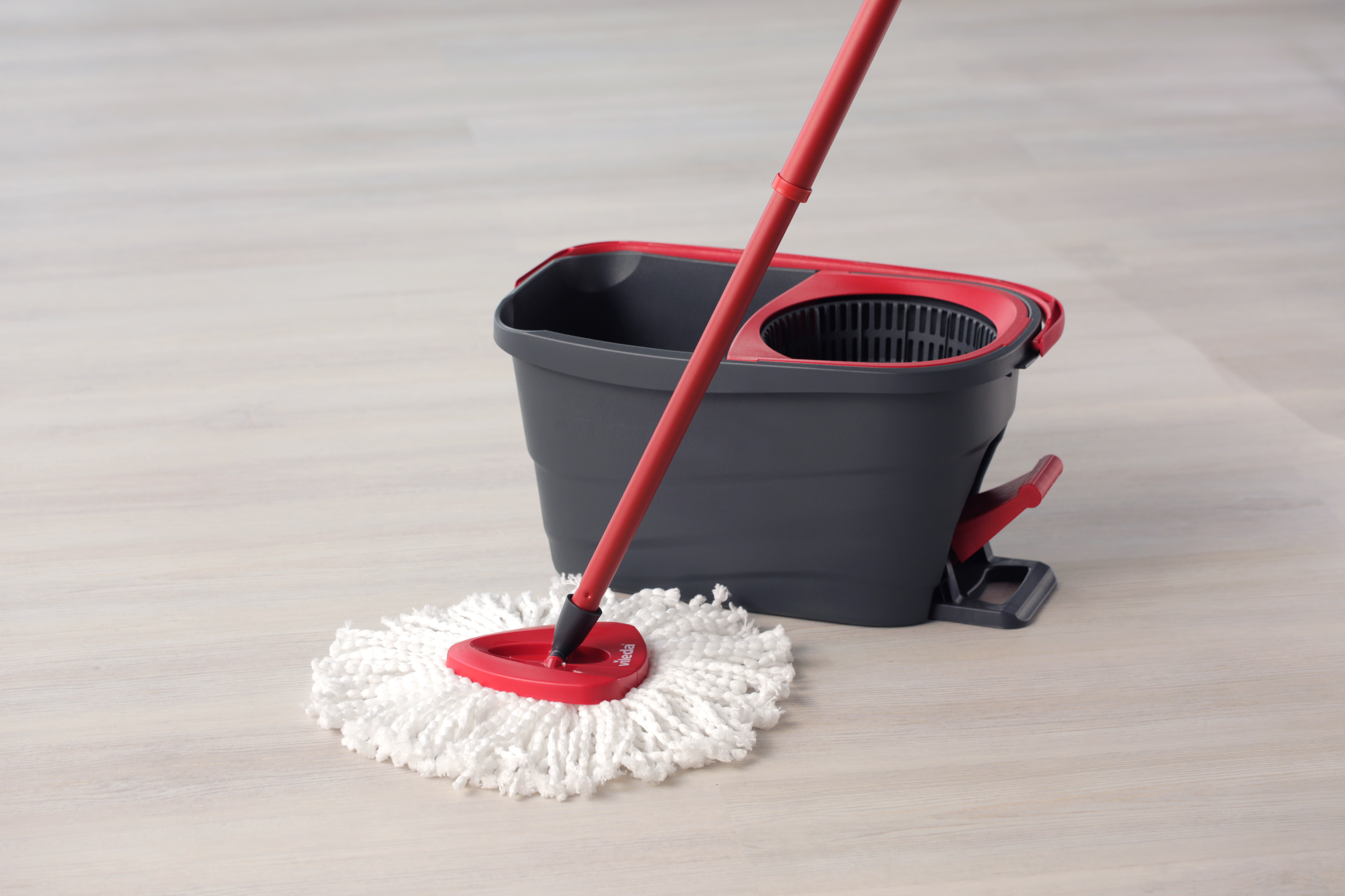 Mop Vileda w użyciu na jasnej drewnianej podłodze, z czerwonym uchwytem i wiadrem.