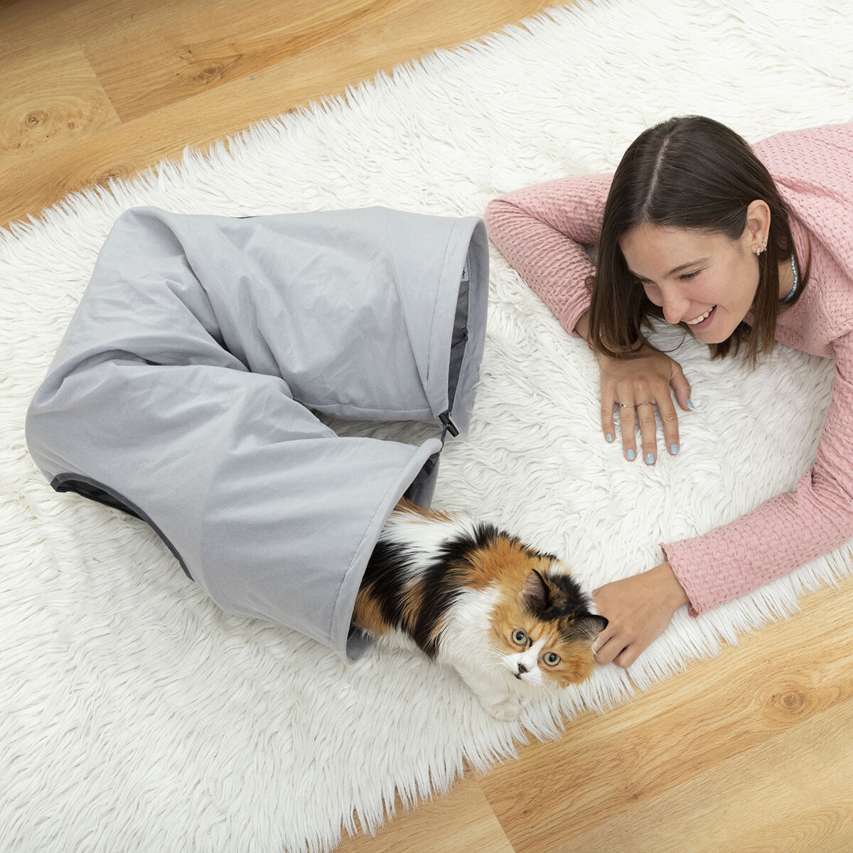 Niña y gato jugando con un túnel gris.