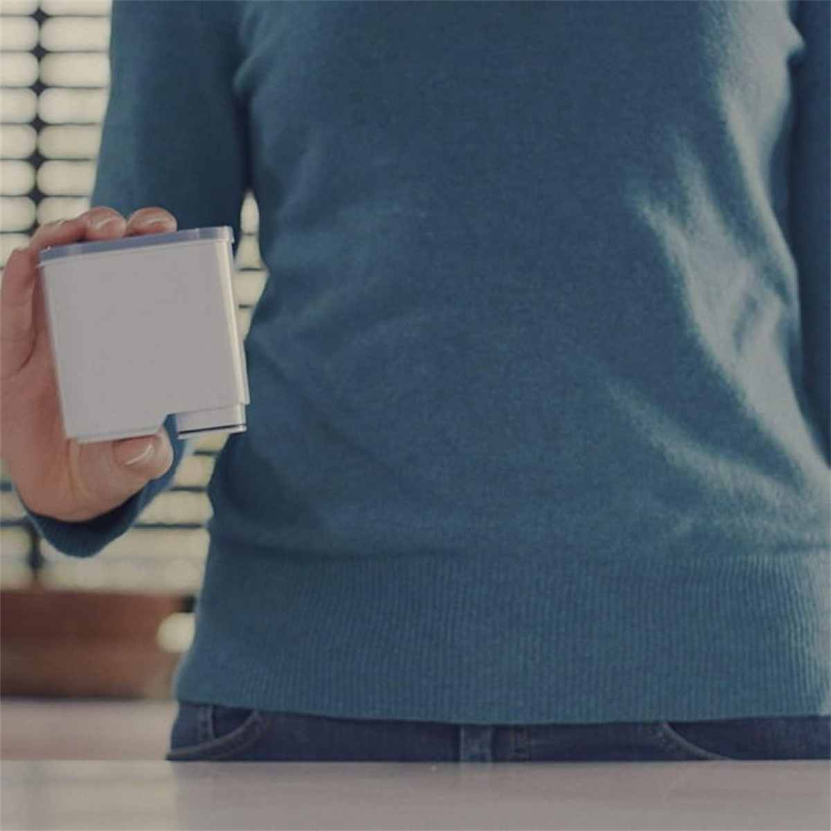Eine Person hält eine weiße Filterkartusche. Sie trägt einen blauen Pullover, der Hintergrund ist neutral.