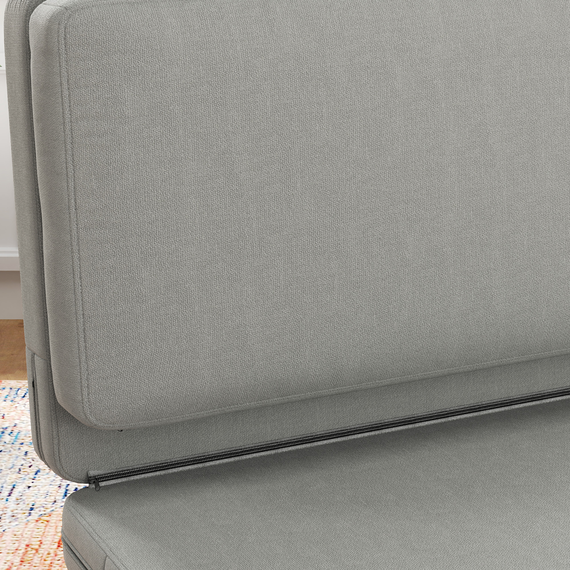 Nahaufnahme eines grauen Klappsofas, der Reißverschluss ist sichtbar. Der Hintergrund ist unscharf.