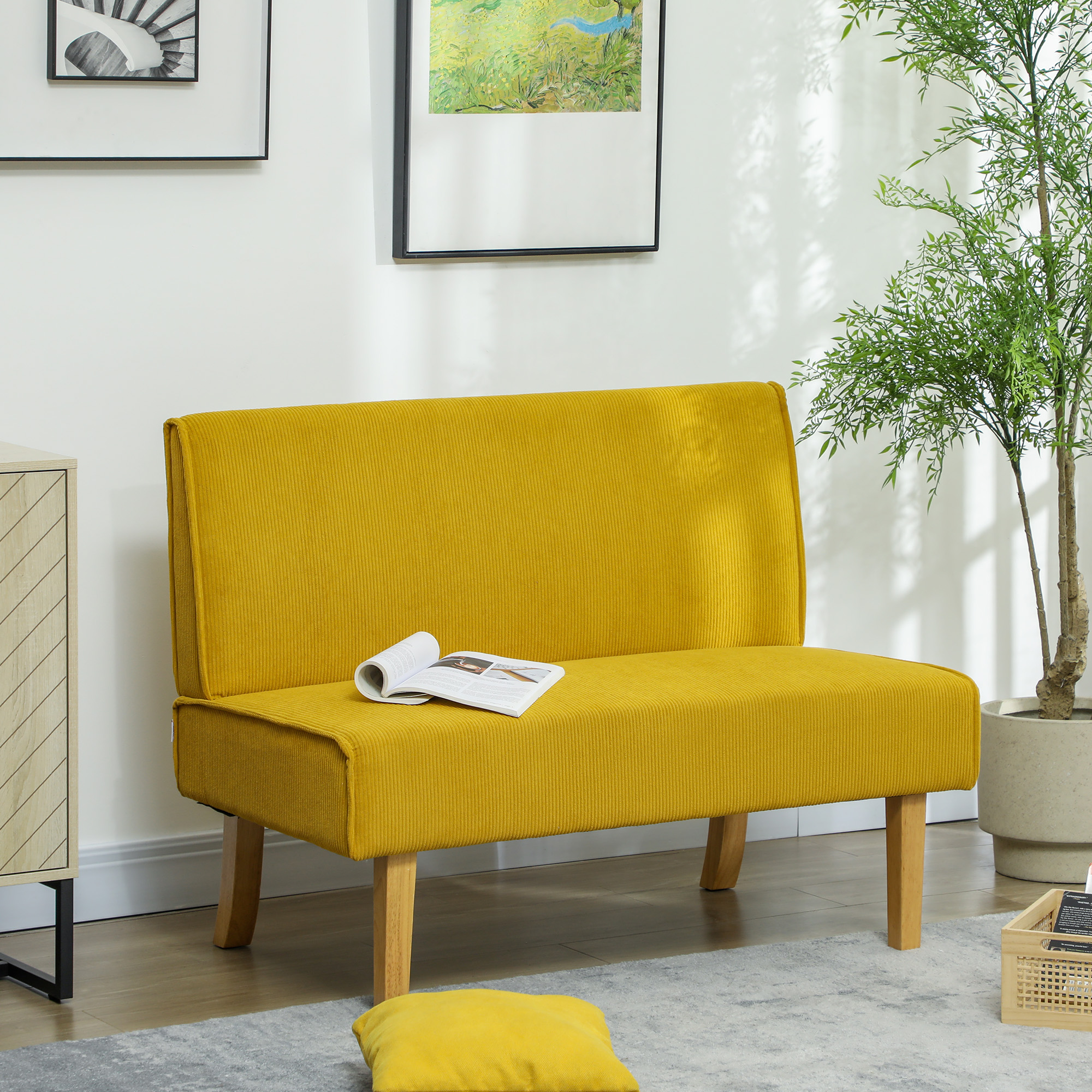 Ein gelbes Cordsofa mit Holzbeinen, einem Buch und einem Kissen in einem Raum.