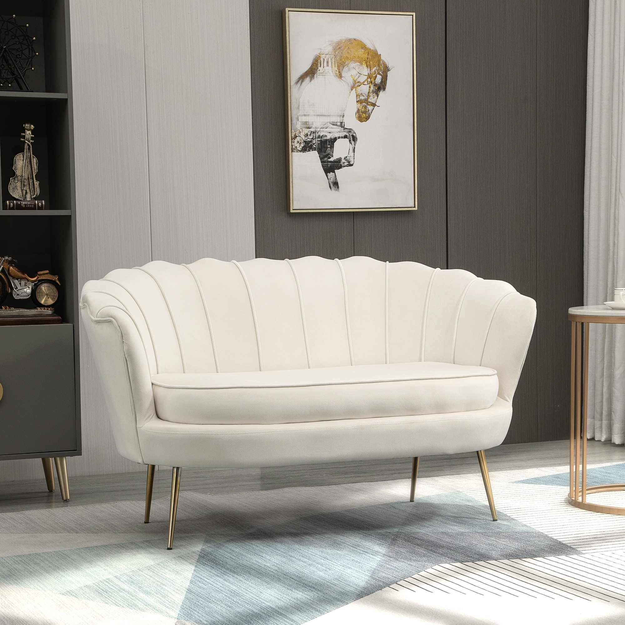 Eine weiße Couch mit goldenen Beinen. Sie steht vor einer grau-weißen Wand und einem blauen Teppich.