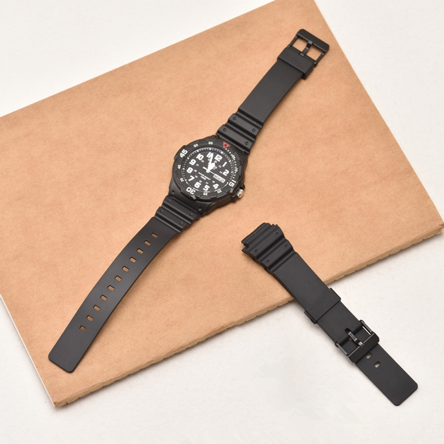 Schwarze Uhr mit schwarzem Armband, auf brauner Oberfläche, mit abgenommenem Armband.