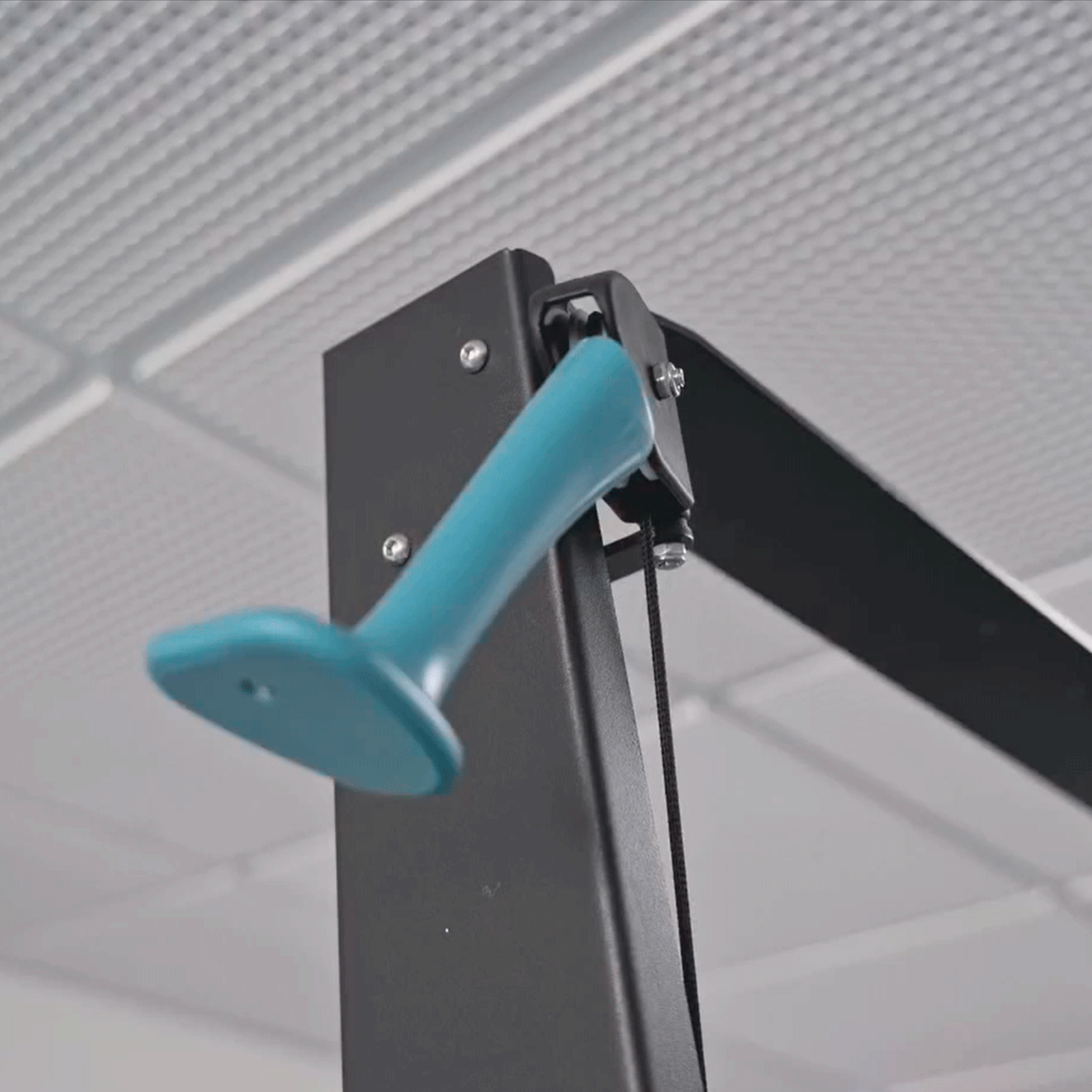 Primer plano de un componente de máquina de gimnasio, con mango turquesa y marco negro, contra techo blanco.