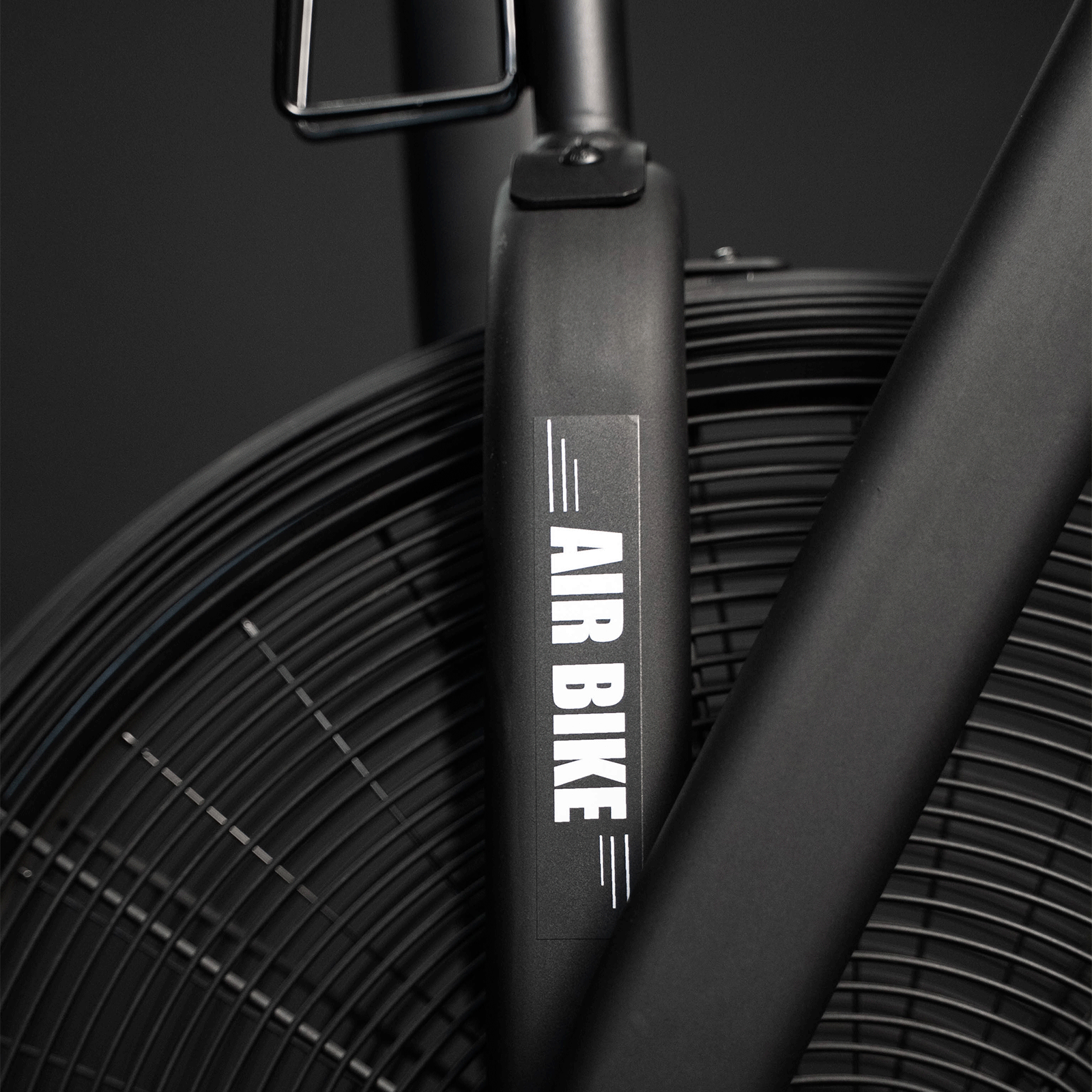 Primo piano di una cyclette ad aria nera con etichetta 'AIR BIKE'. Sfondo nero.