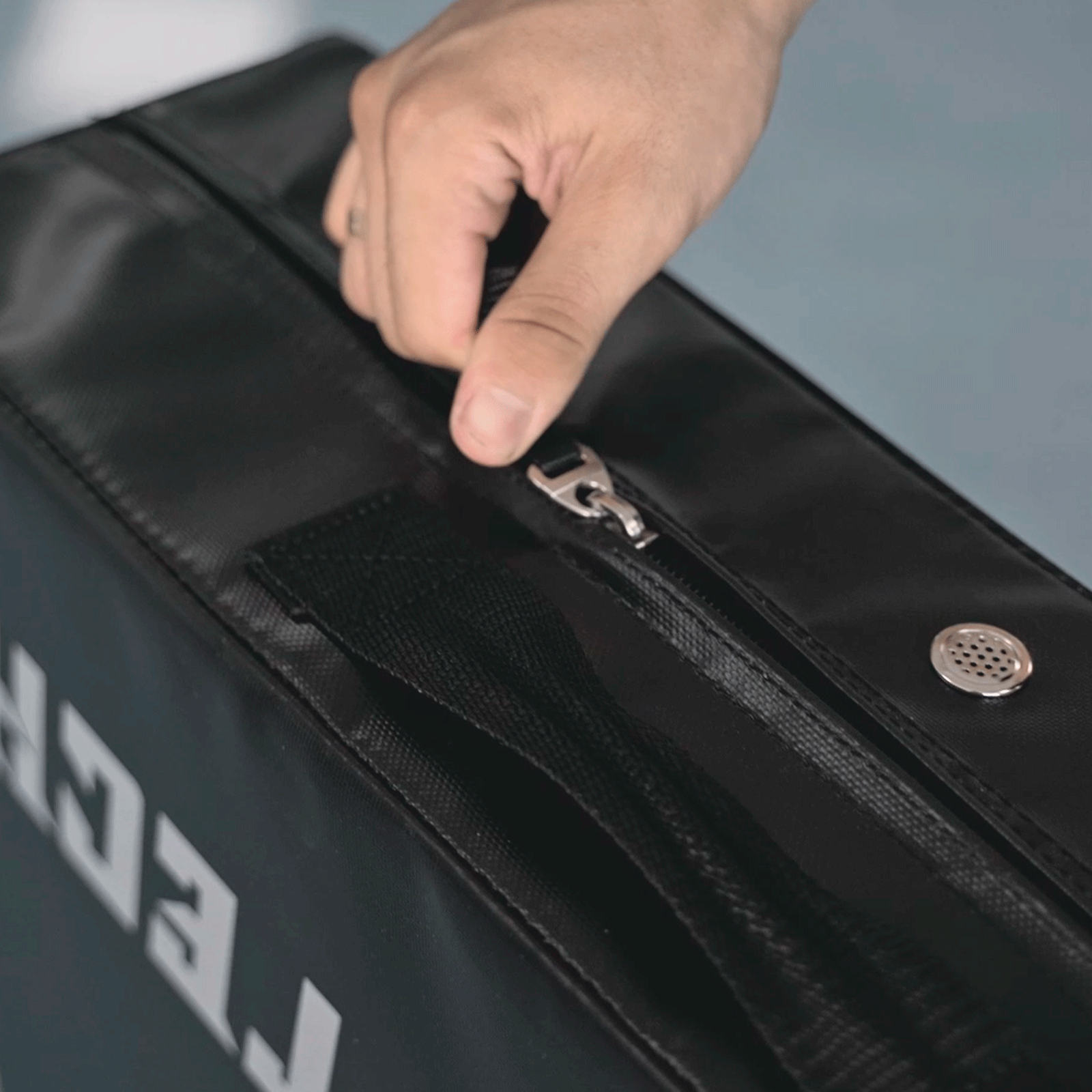 Una mano cierra una bolsa negra con cremallera. La bolsa tiene el texto FITNESS TECH.