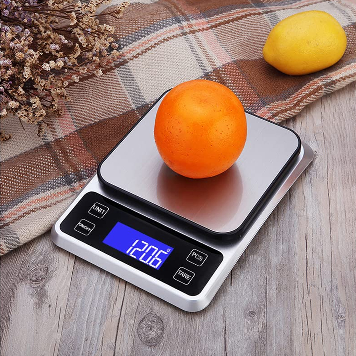 Eine Digitalwaage mit einer Orange darauf und Zitrone in der Nähe. Das Display zeigt 1206. Die Waage steht auf Holz.