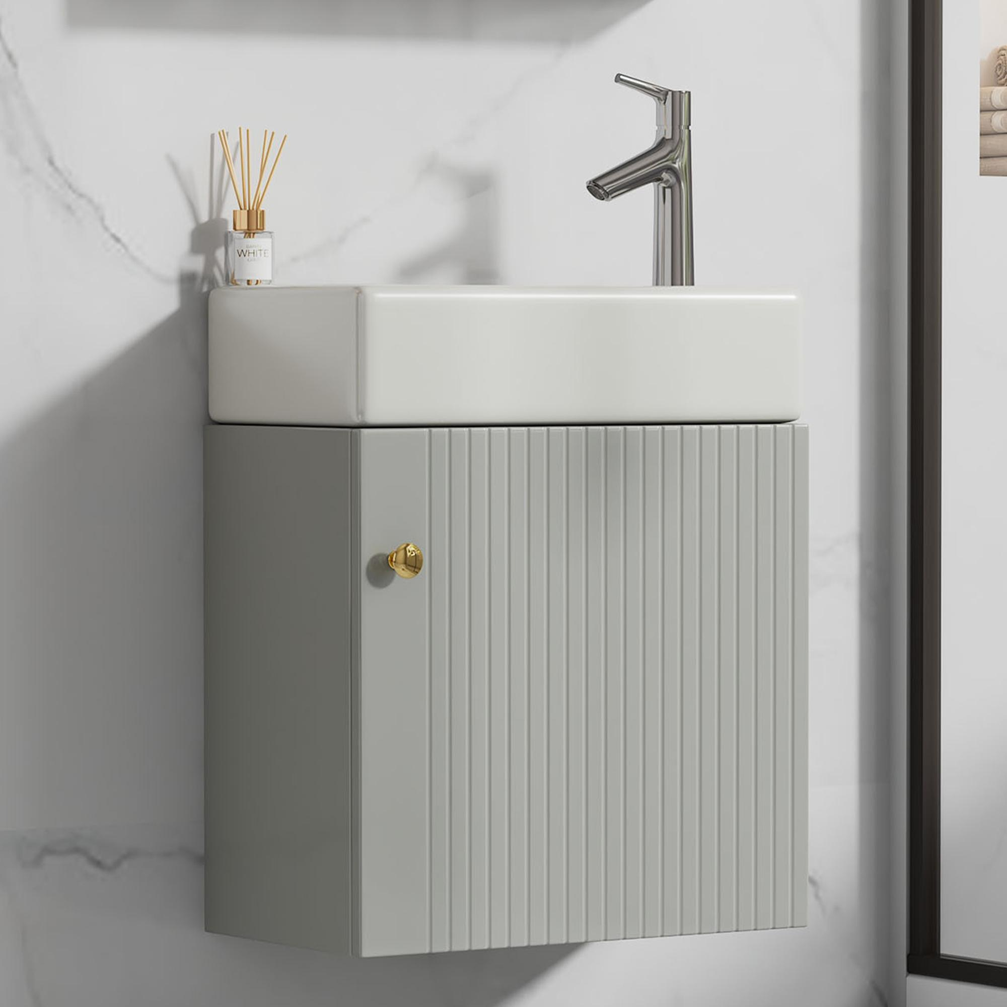 Ein weißes rechteckiges Waschbecken auf einem grauen Schrank mit goldenem Knauf. Über dem Waschbecken befindet sich ein Wasserhahn.