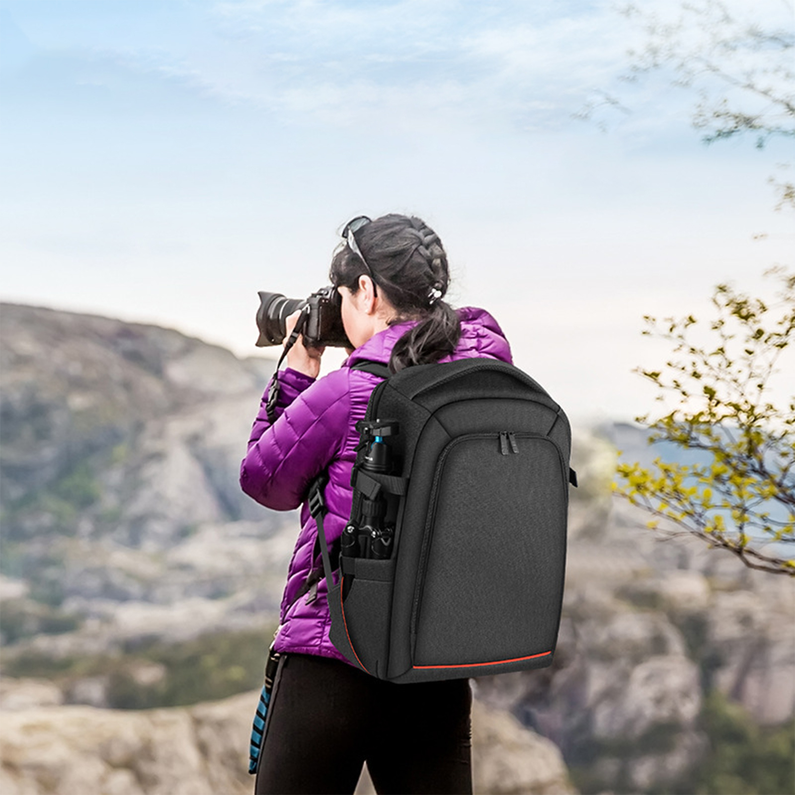 Eine Person mit Rucksack macht ein Foto mit einer Kamera. Ein malerischer Berg-Hintergrund ist sichtbar.