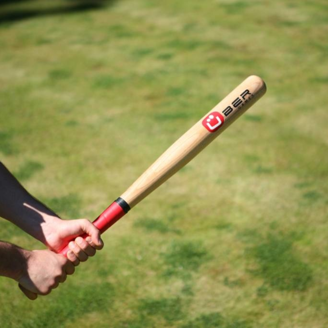 Ein Baseballschläger wird von Händen gehalten, mit grünem Gras im Hintergrund.
