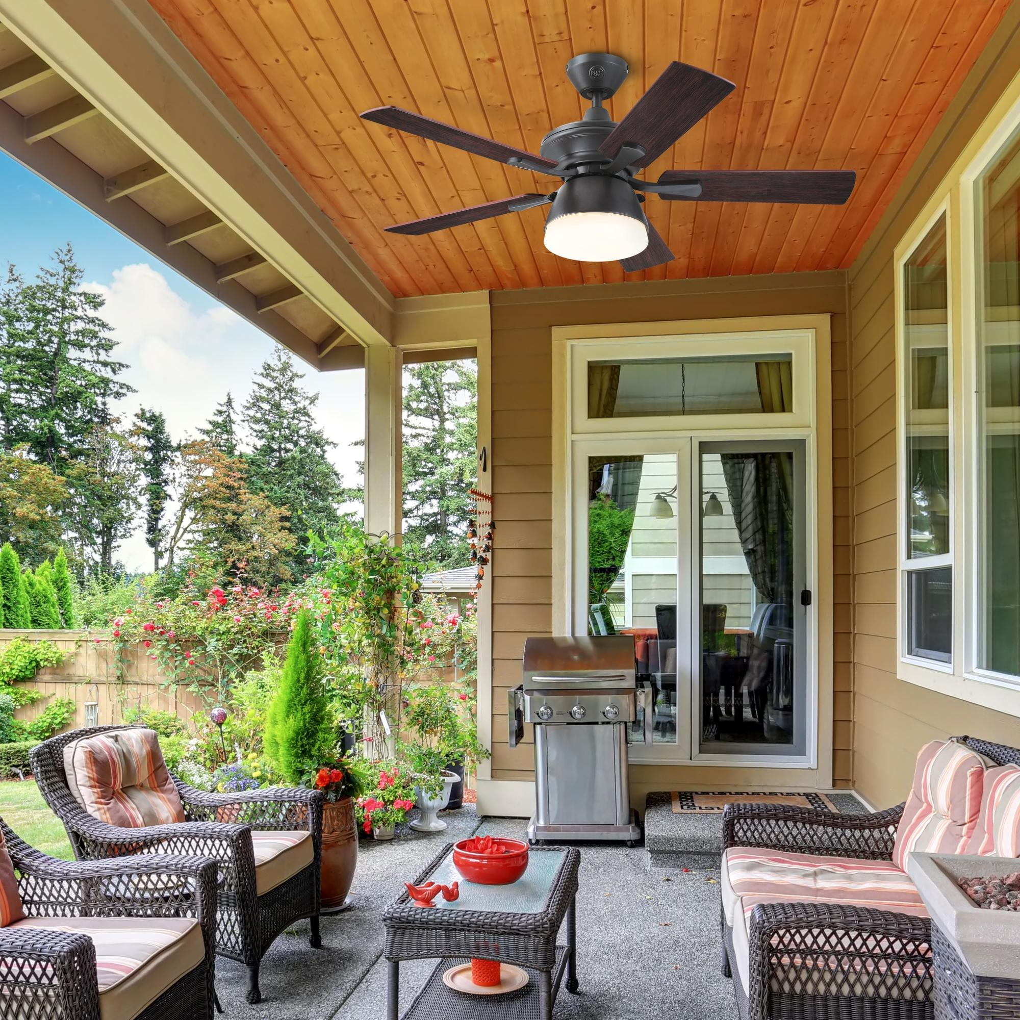 Terrasse mit Deckenventilator, Gartenmöbeln, Grill und Blick auf einen Garten und Bäume.