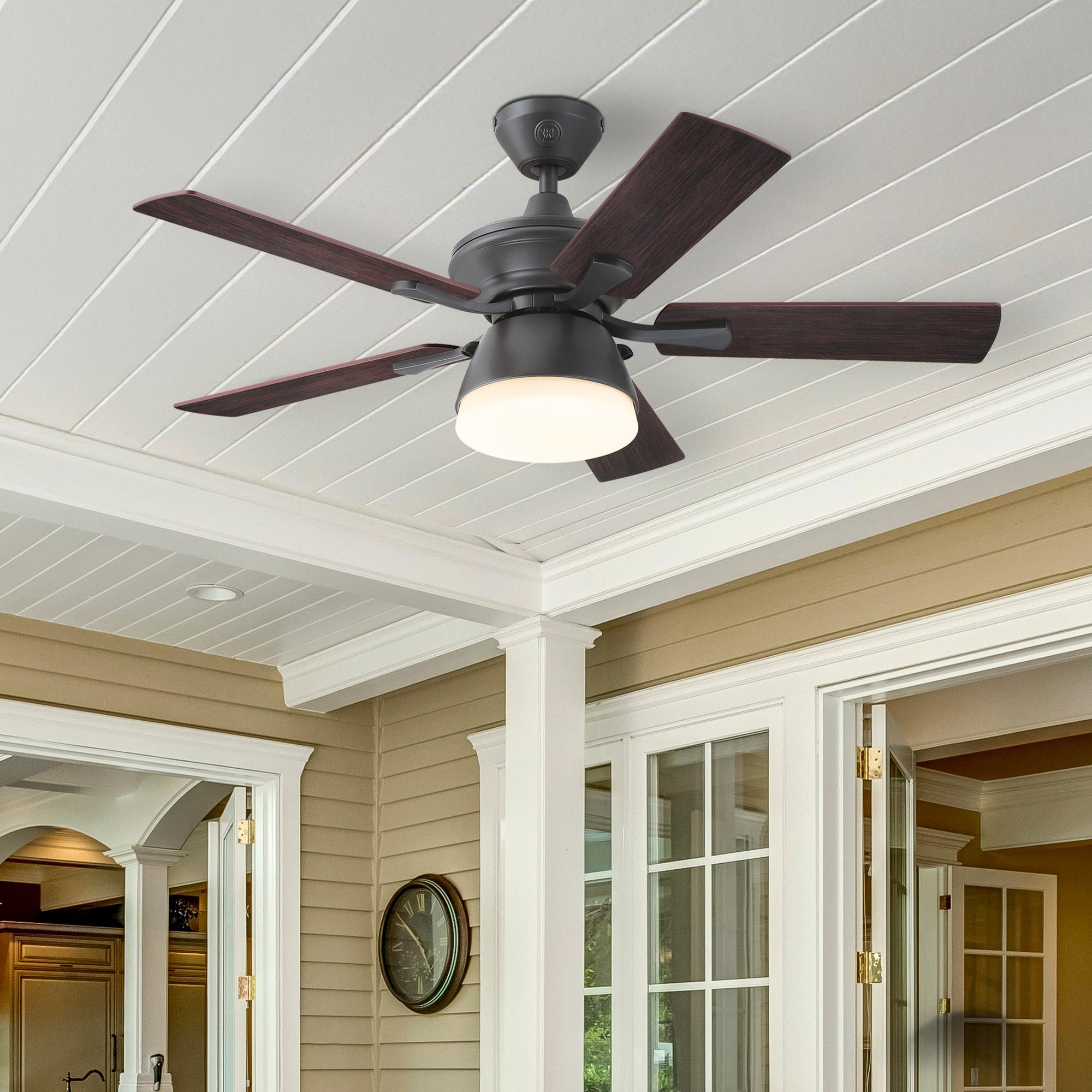 Deckenventilator mit dunkelbraunen Flügeln, weiße Decke und beige Wand, offene Türen und Fenster.