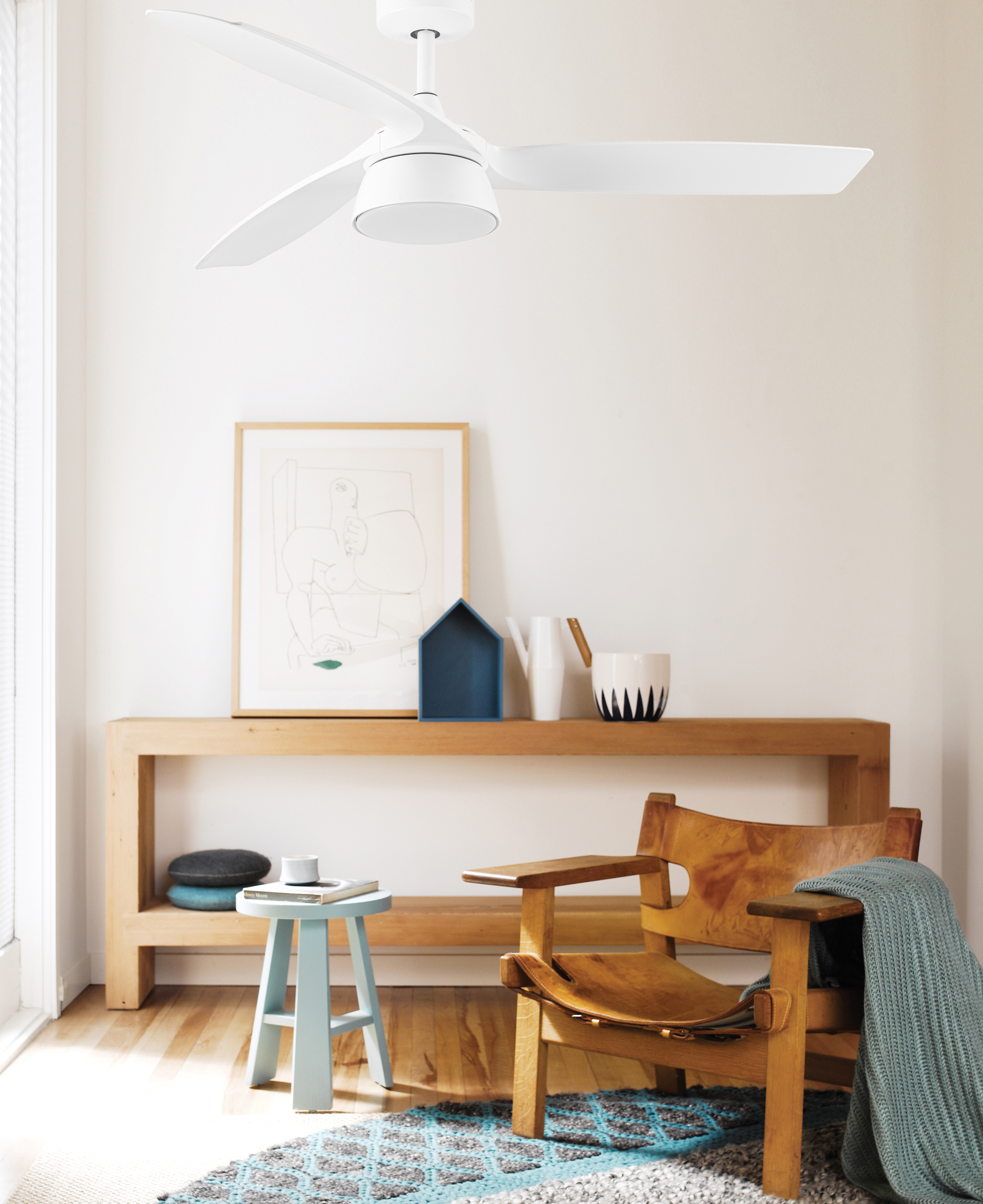Innenraum mit Deckenventilator, Holzbank, Stuhl und Kunst. Der Raum hat eine helle Innenausstattung.