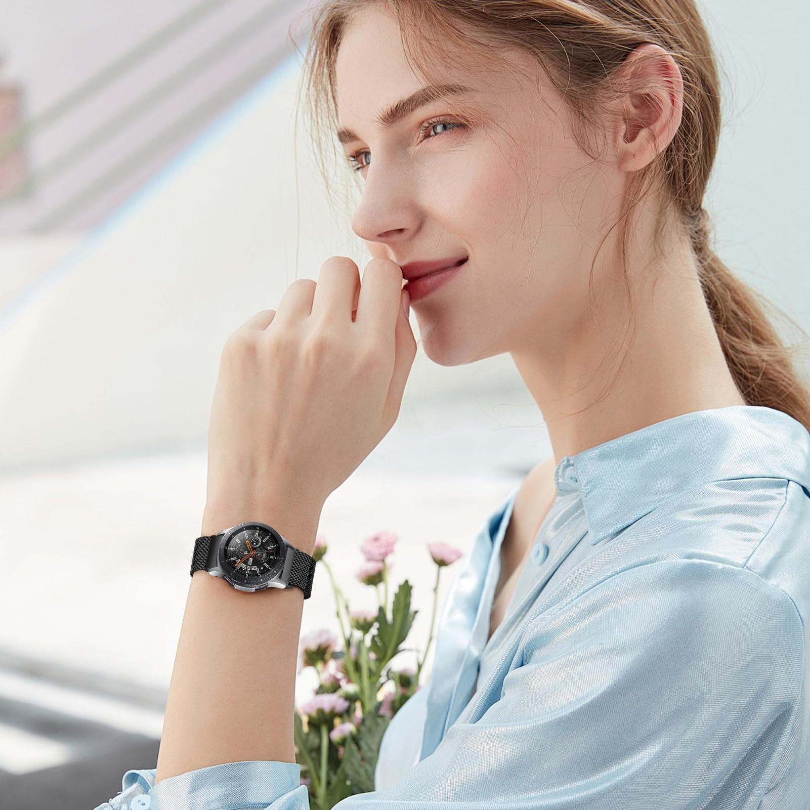 Una donna con un orologio, camicia azzurra, guarda a destra, sorridendo leggermente.