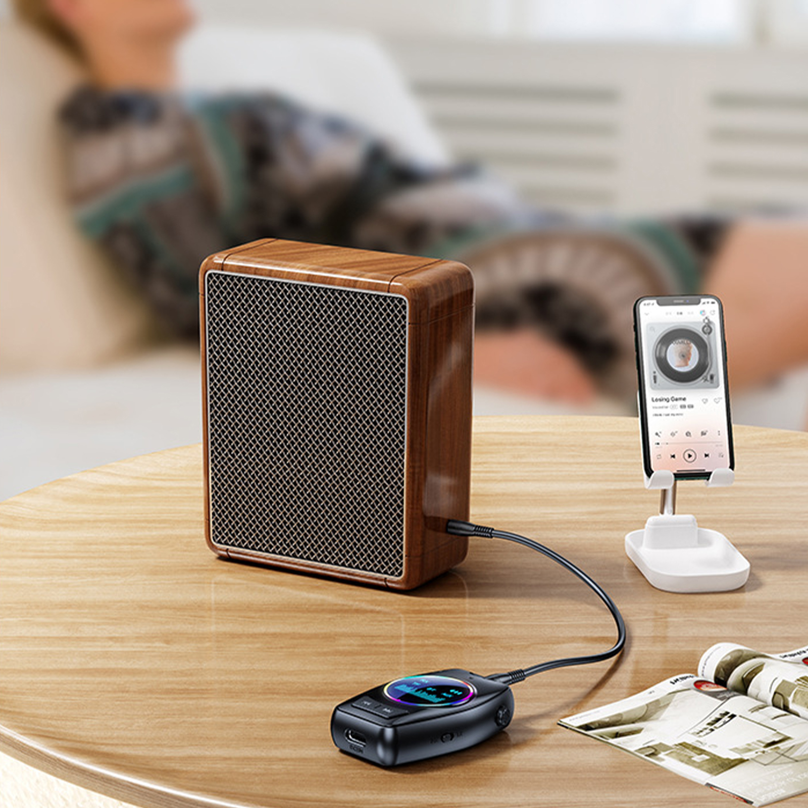 Holz-Lautsprecher und Audiogerät, durch ein Kabel verbunden. Person entspannt im Hintergrund.