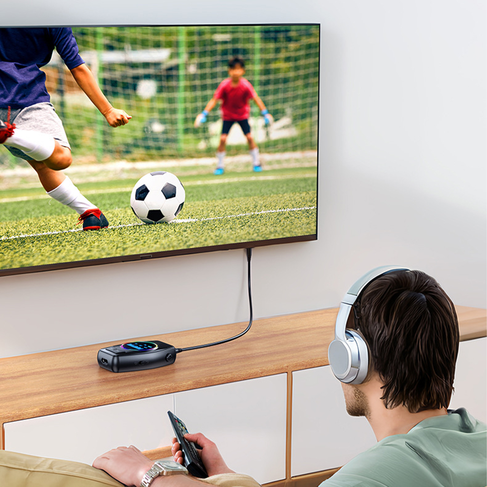 Person mit Kopfhörern schaut fern. Ein Fußballspiel läuft im Fernsehen. Ein Audiogerät auf dem Tisch.