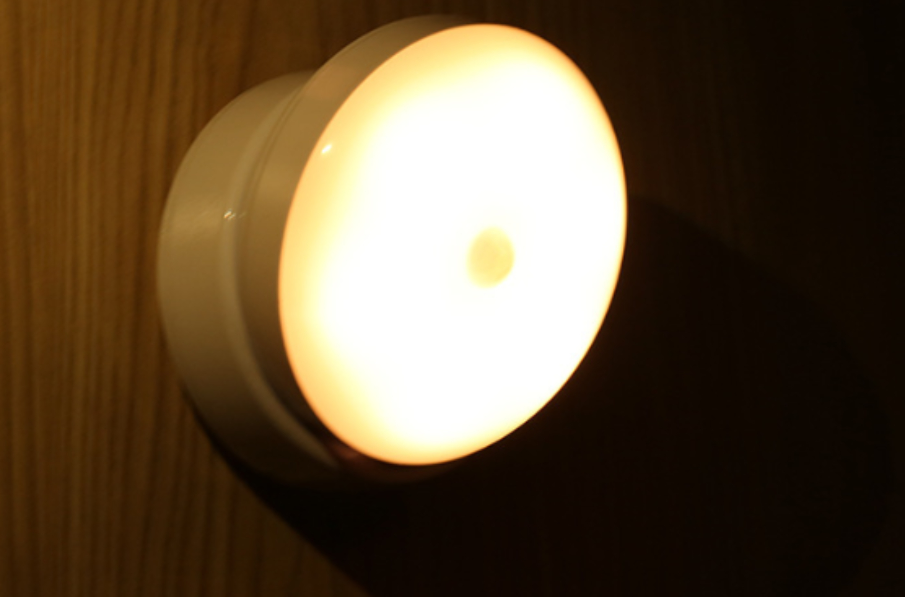 Ein weißes Nachtlicht an einer Holzwand. Es strahlt ein helles Licht aus.