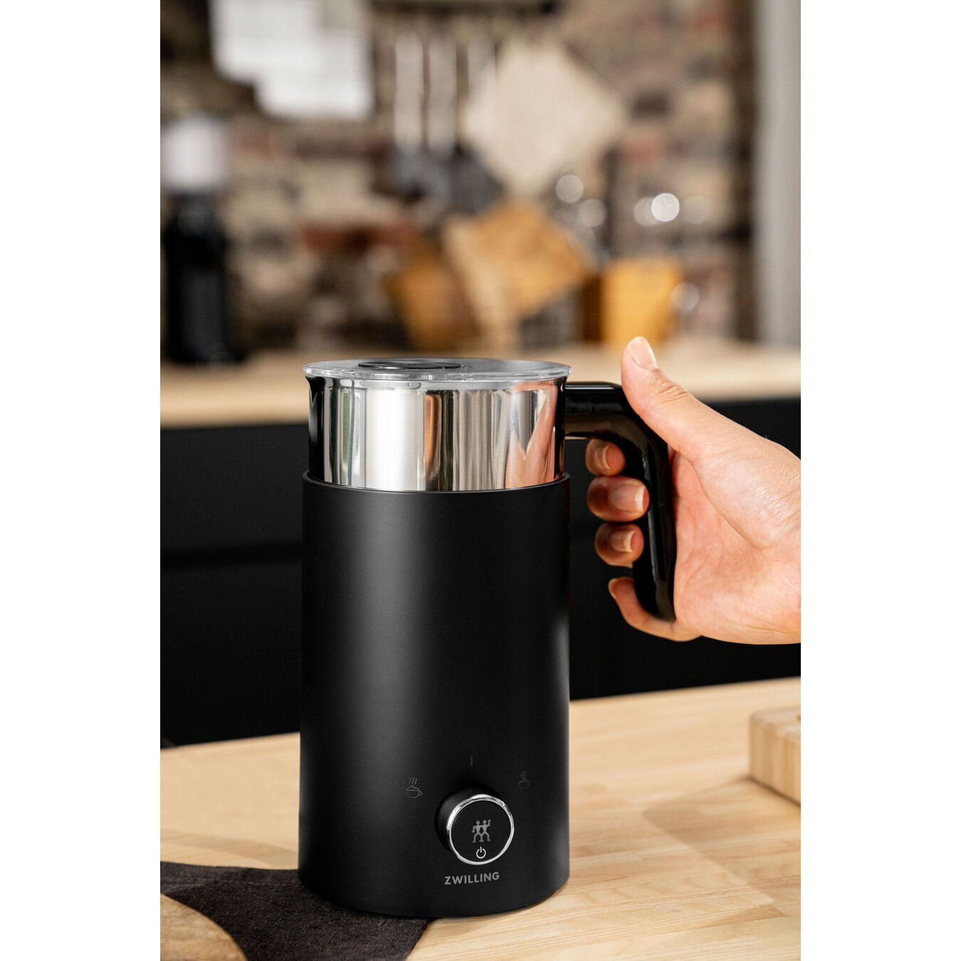 Czarny i srebrny spieniacz do mleka na drewnianym stole, dłoń trzymająca uchwyt.