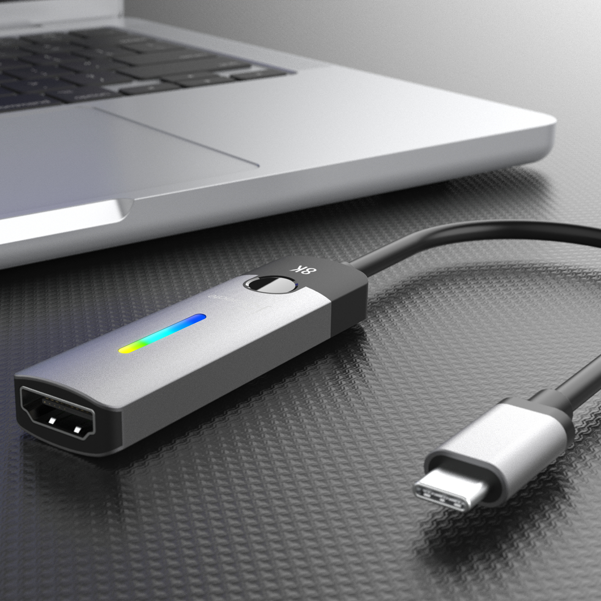 Silberner Adapter, der an einen Laptop und einen Monitor auf einer strukturierten Oberfläche angeschlossen ist.