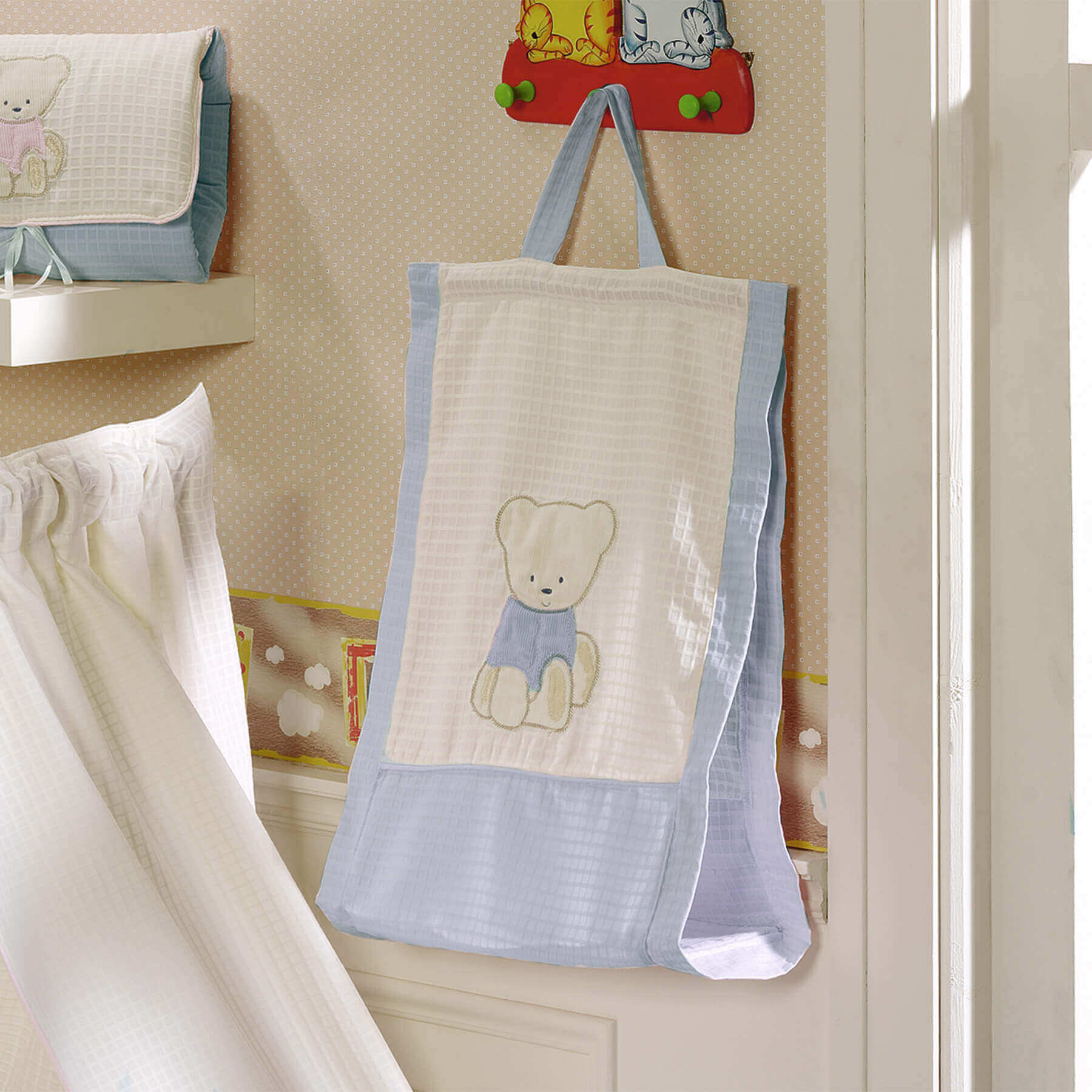 Bolso de bebé colgado en la pared, con diseño de osito. Colores azul claro y blanquecino.