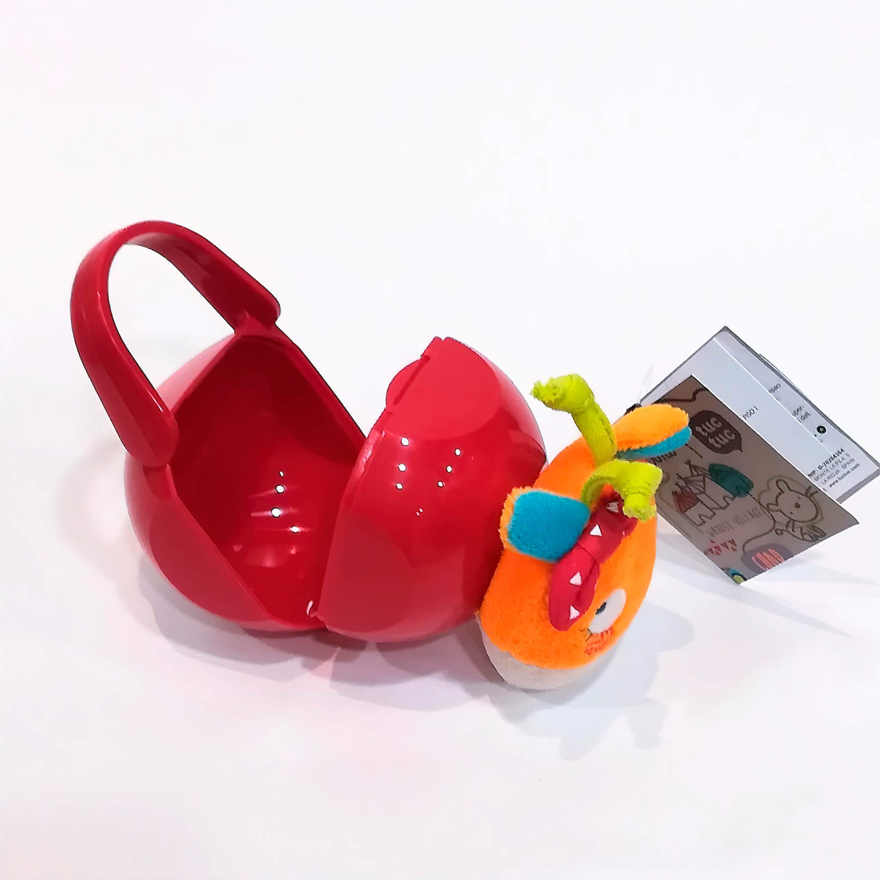 Un juguete de plástico rojo en forma de esfera se abre para revelar un juguete de monstruo. Fondo blanco.