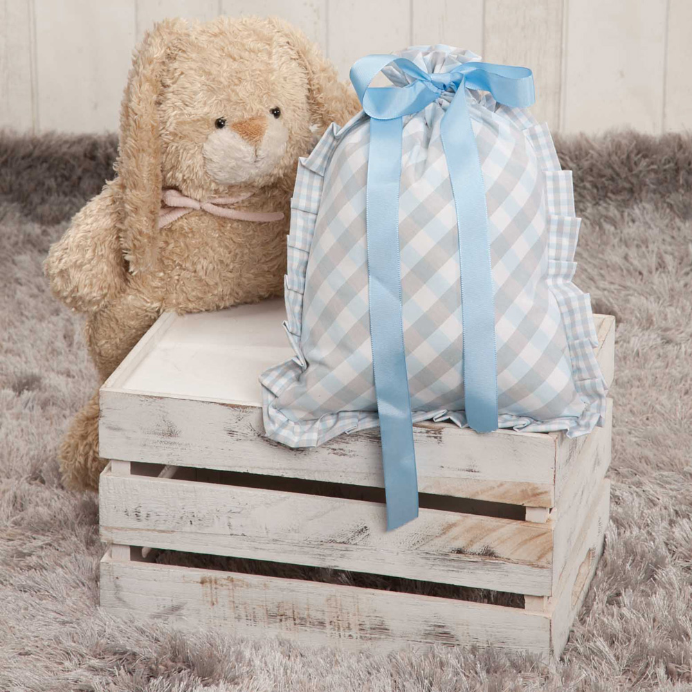 Caja de madera blanca con un oso de peluche y una bolsa con cintas azules sobre una alfombra gris.