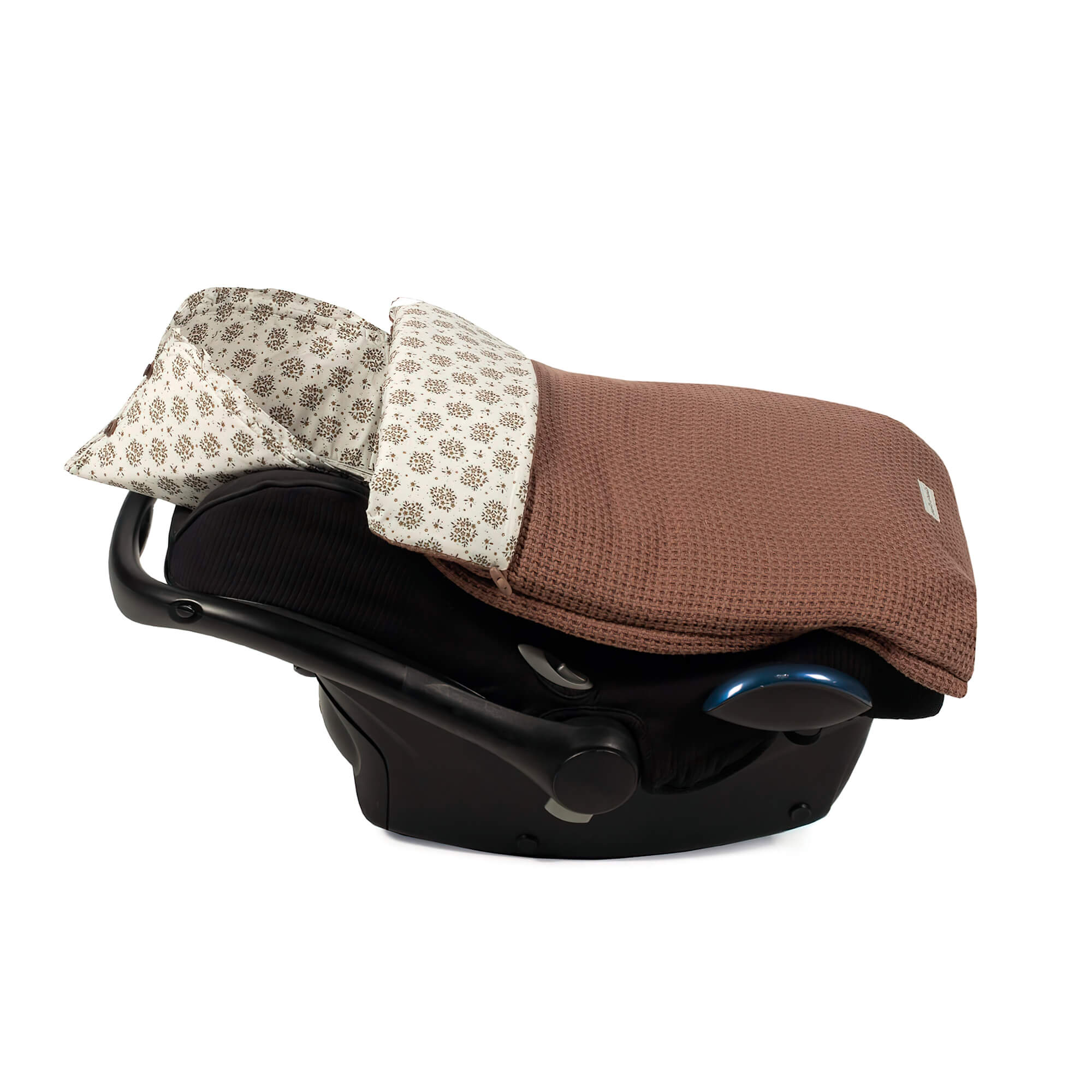 Saco de dormir marrón para bebé en un asiento de coche. La capucha es blanca y marrón estampada.