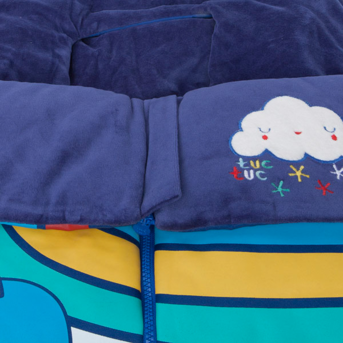 Saco de dormir azul para bebé con estampado de nubes y estrellas. Cremallera en el centro, rayas de varios colores.