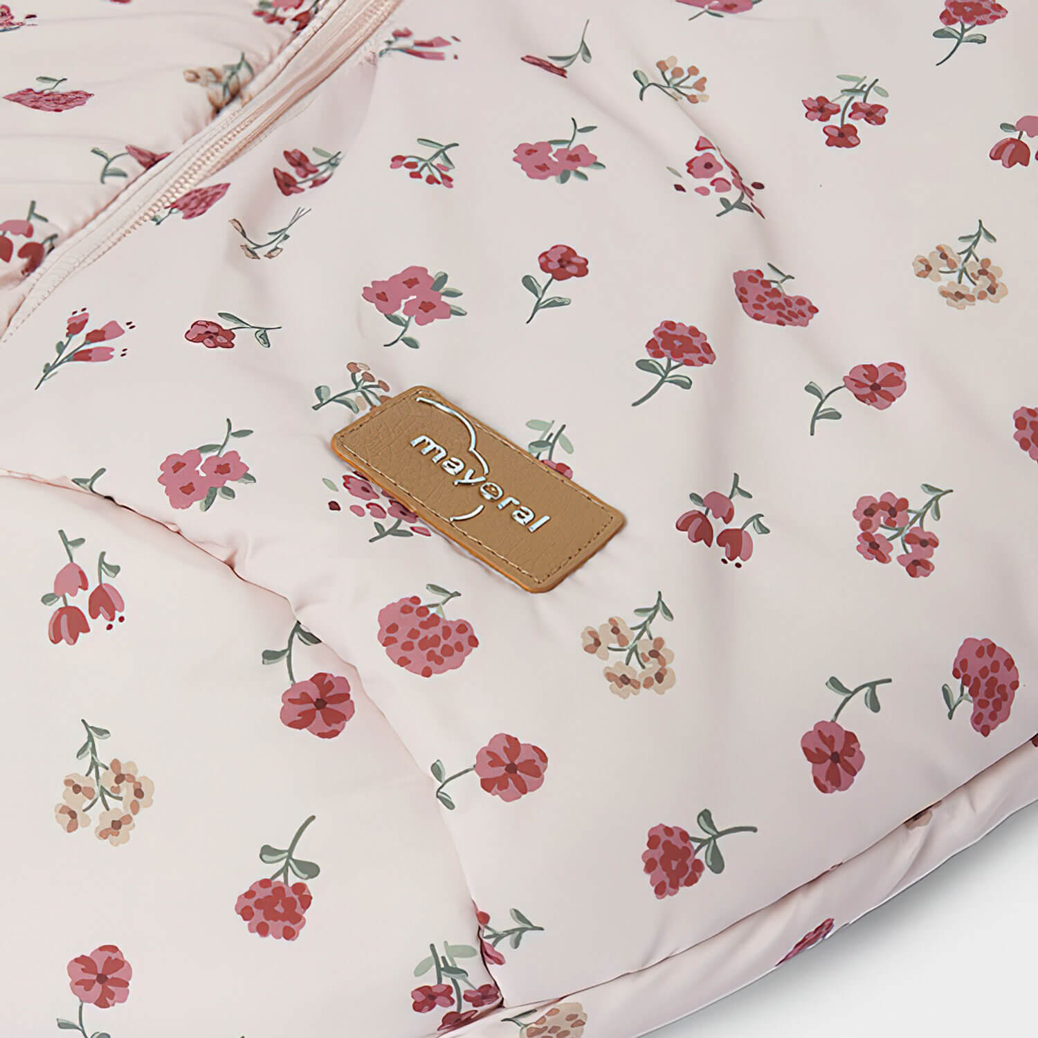 Un saco de dormir para bebé con estampado floral y etiqueta marrón sobre fondo blanco.