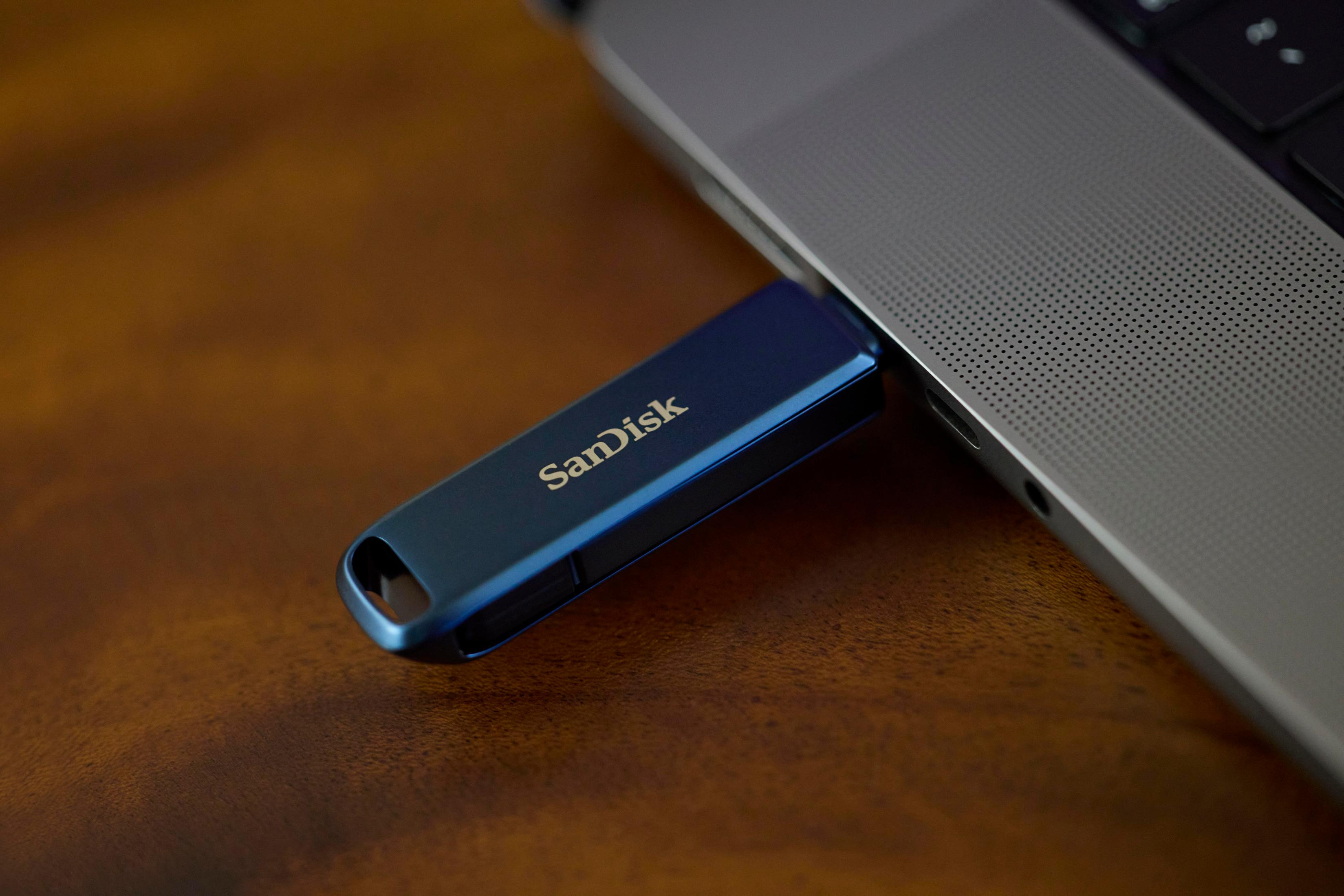 Clé USB SanDisk bleue branchée sur un ordinateur portable. La clé USB est sur une table en bois.