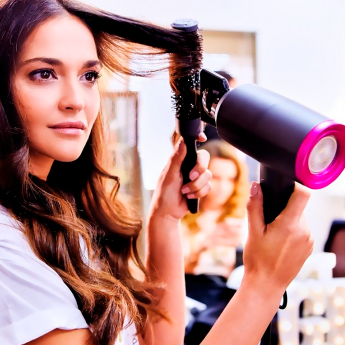 Una mujer peinando su cabello con un secador y un cepillo redondo.