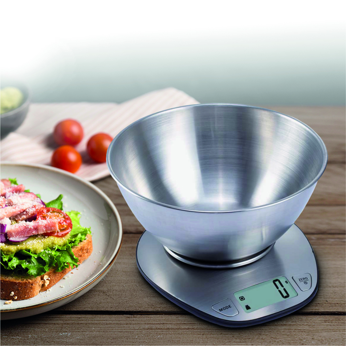 Un cuenco de acero inoxidable sobre una báscula de cocina digital con comida cerca.