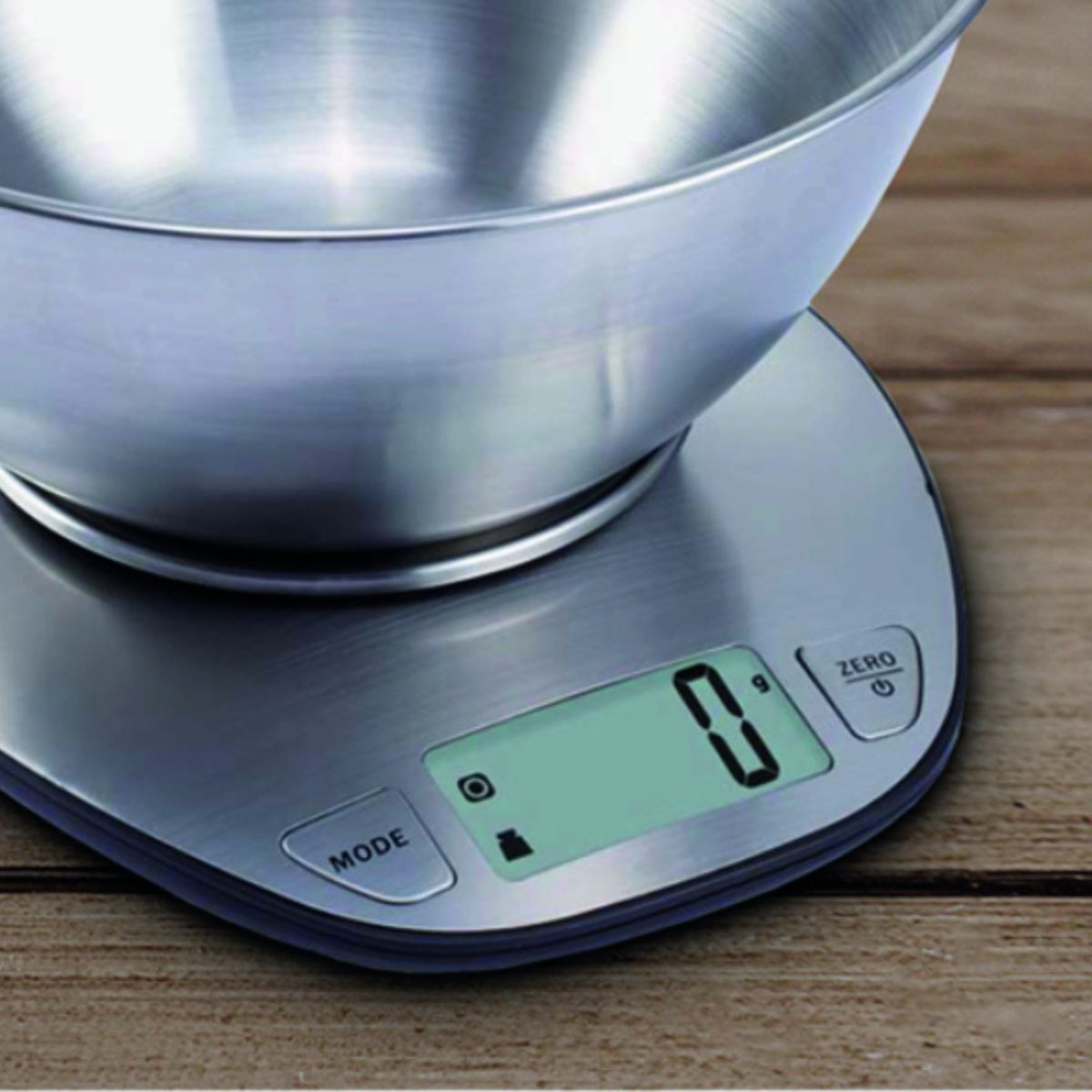 Una báscula de cocina digital con un cuenco de acero inoxidable sobre una superficie de madera.