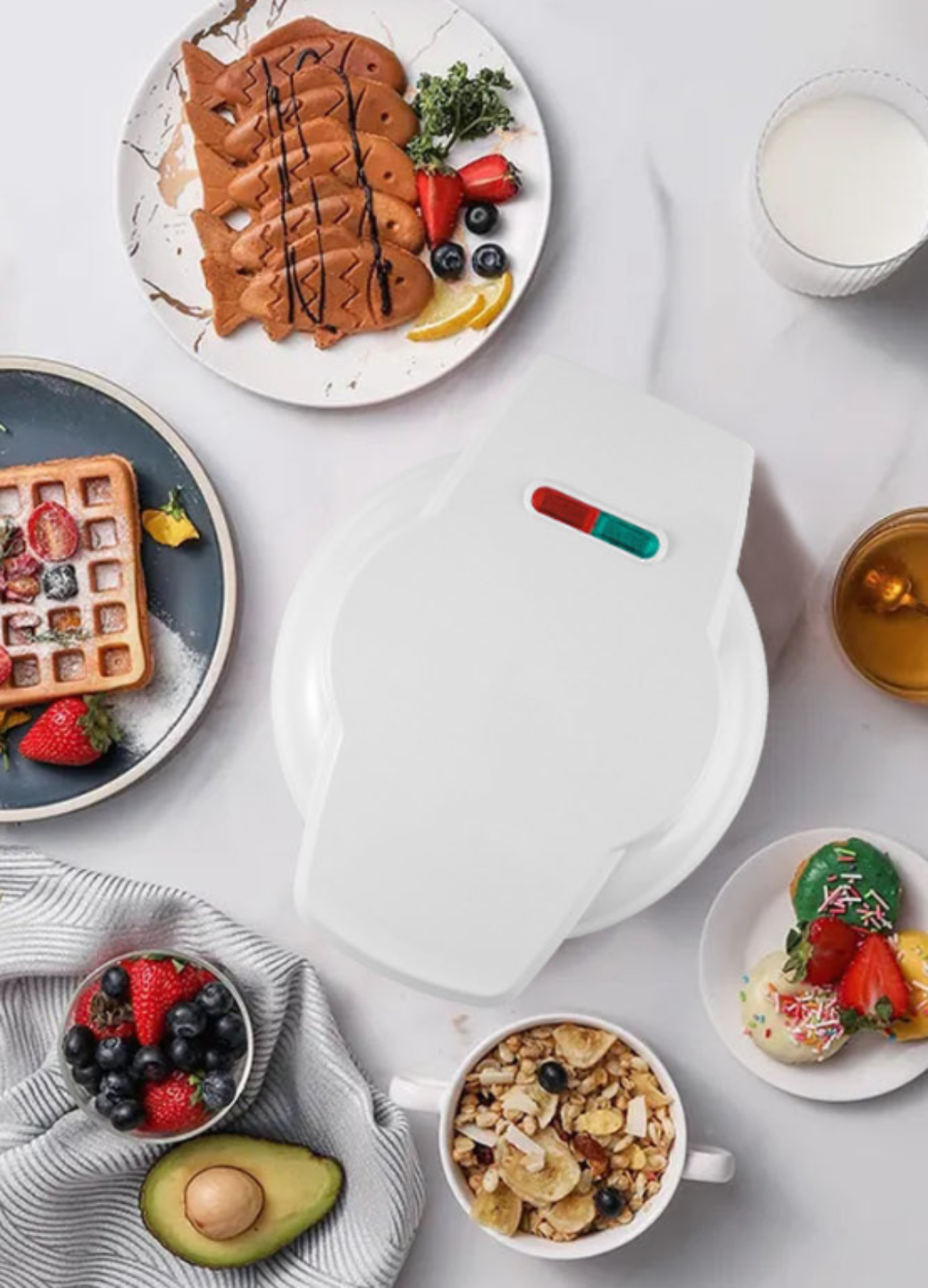 Weißer Waffeleisen mit Waffeln, Früchten und anderen Frühstückszutaten auf weißer Oberfläche.