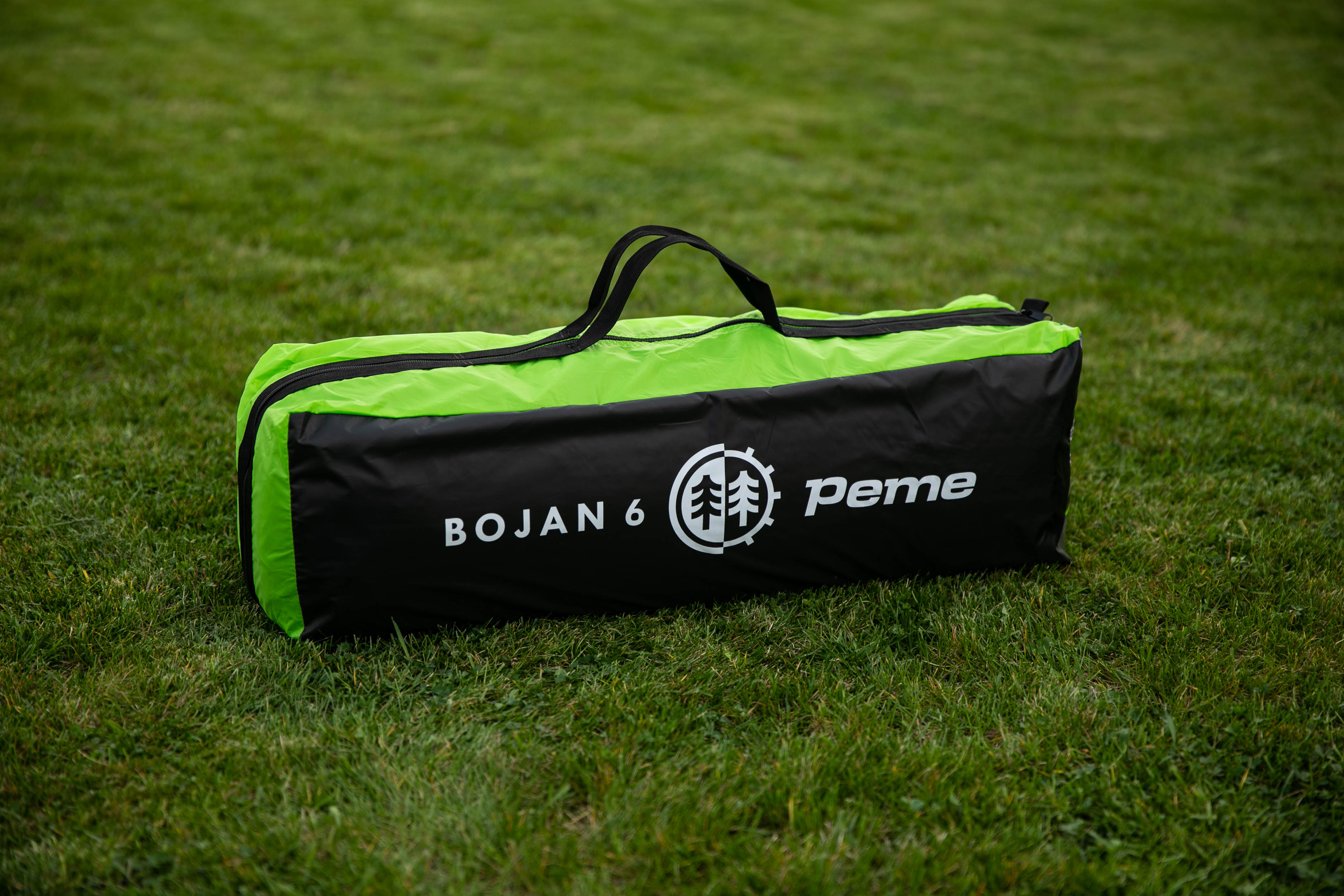 Una bolsa de tienda plegada negra y verde con la etiqueta 'BOJAN 6' sobre hierba verde.