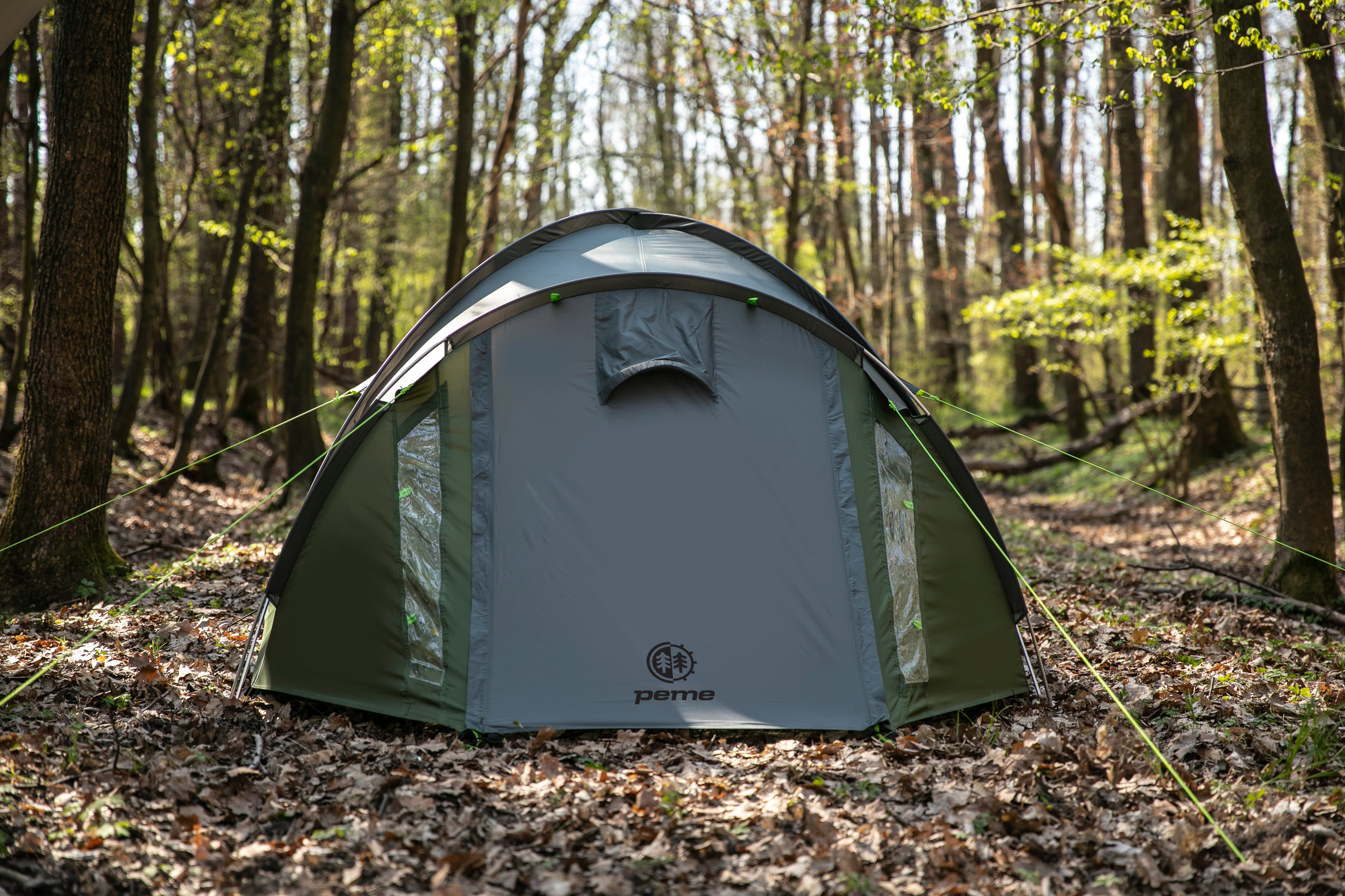 Una tienda de campaña gris y verde instalada en un bosque con árboles al fondo.
