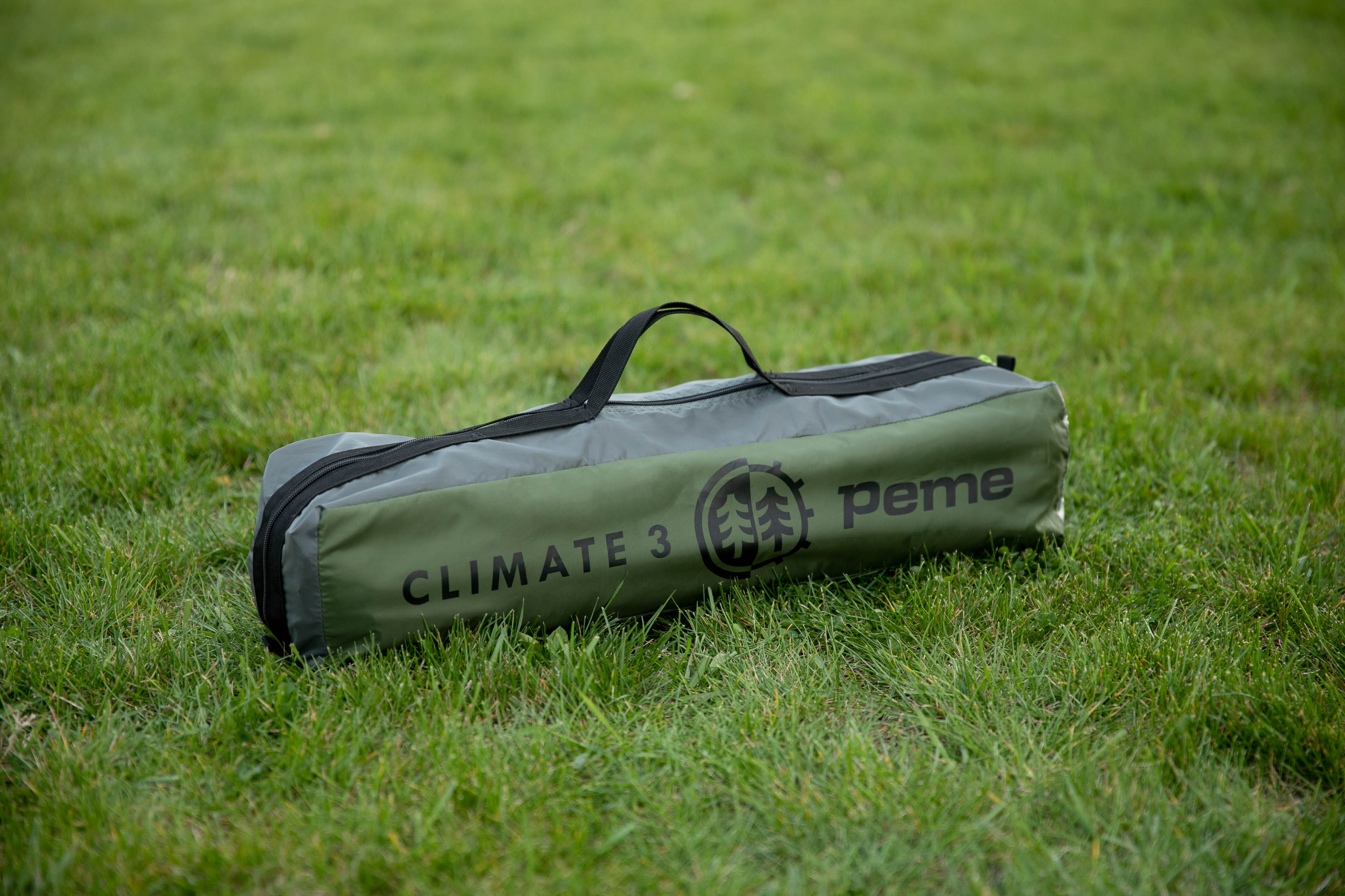Tienda de campaña verde y gris en una bolsa de transporte, colocada sobre hierba verde.