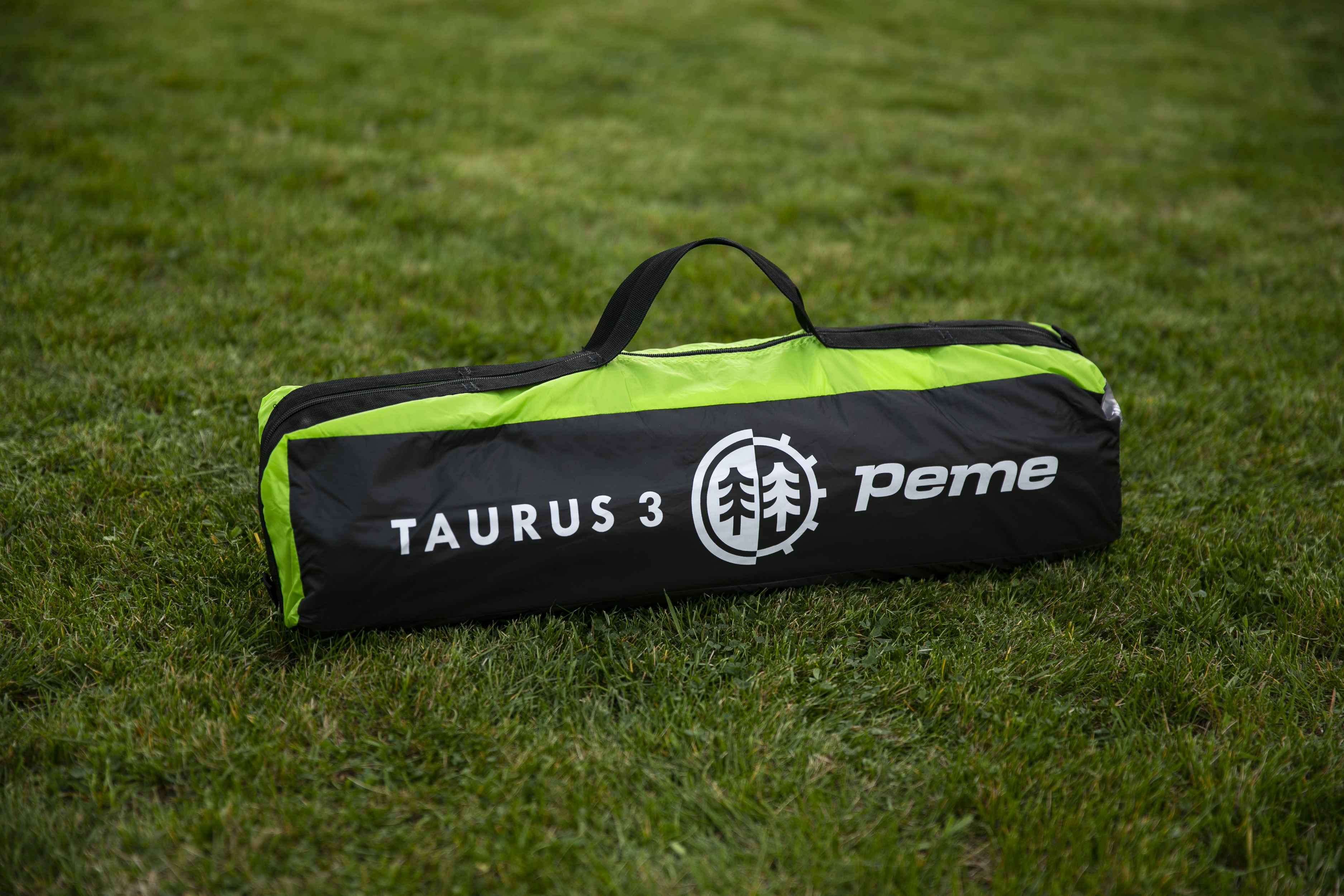 Una bolsa de tienda plegada negra y verde con la etiqueta 'TAURUS 3' sobre hierba verde.