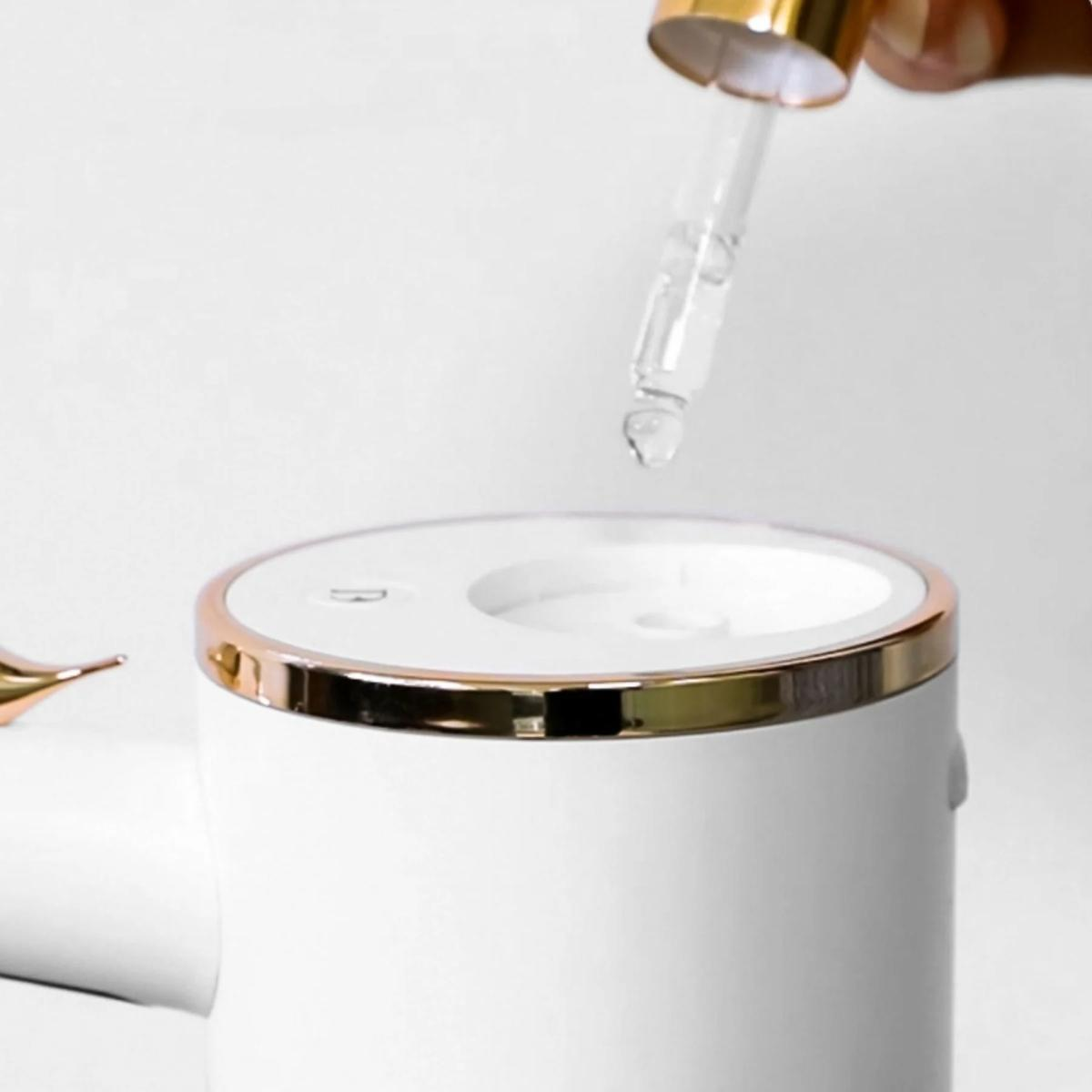 Hand hält eine Pipette über einem weißen Produkt mit goldenem Rand, Pipette gibt Flüssigkeit ab.