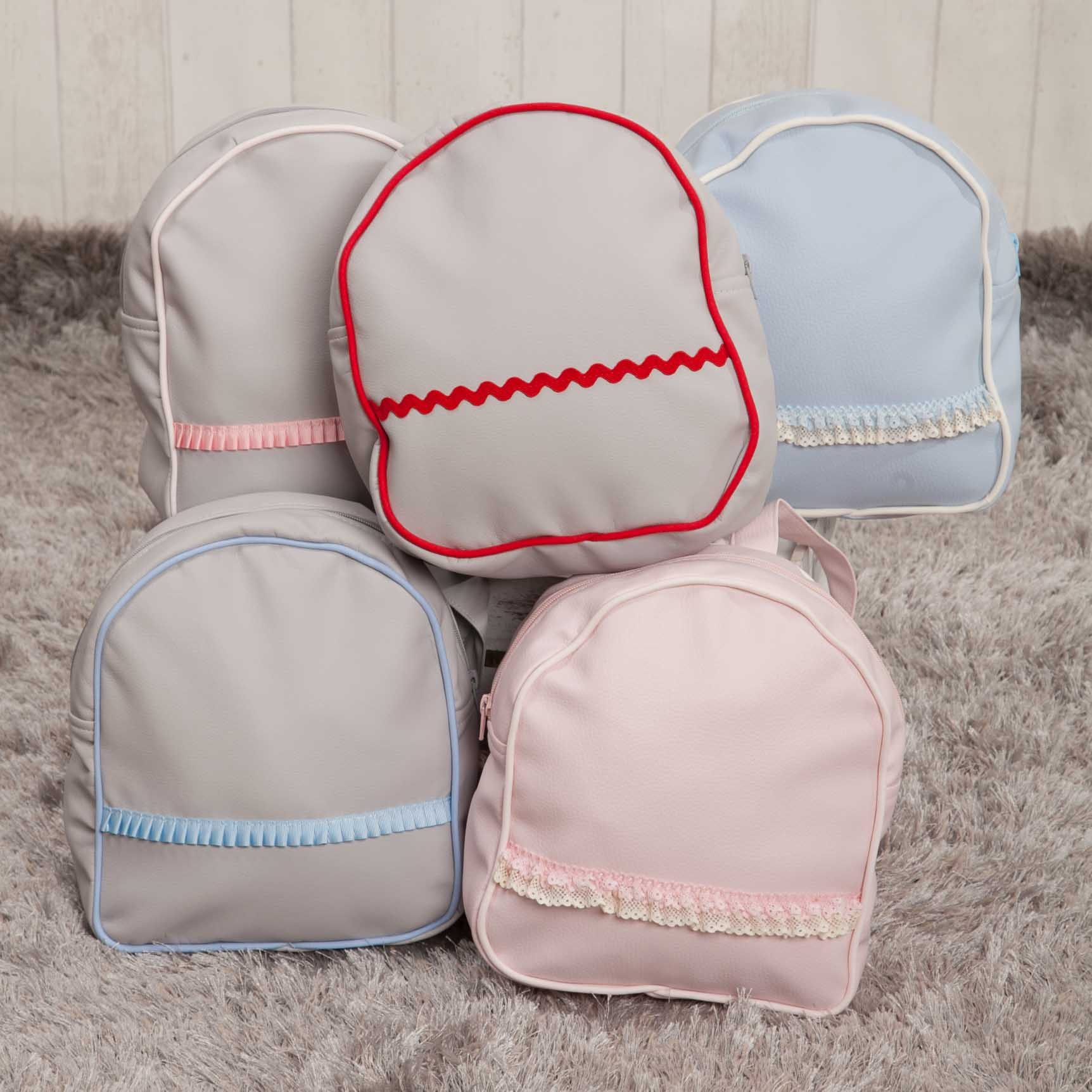 Cinco mochilas pequeñas en diferentes colores: gris, azul claro y rosa. Decoradas con encaje y cintas.