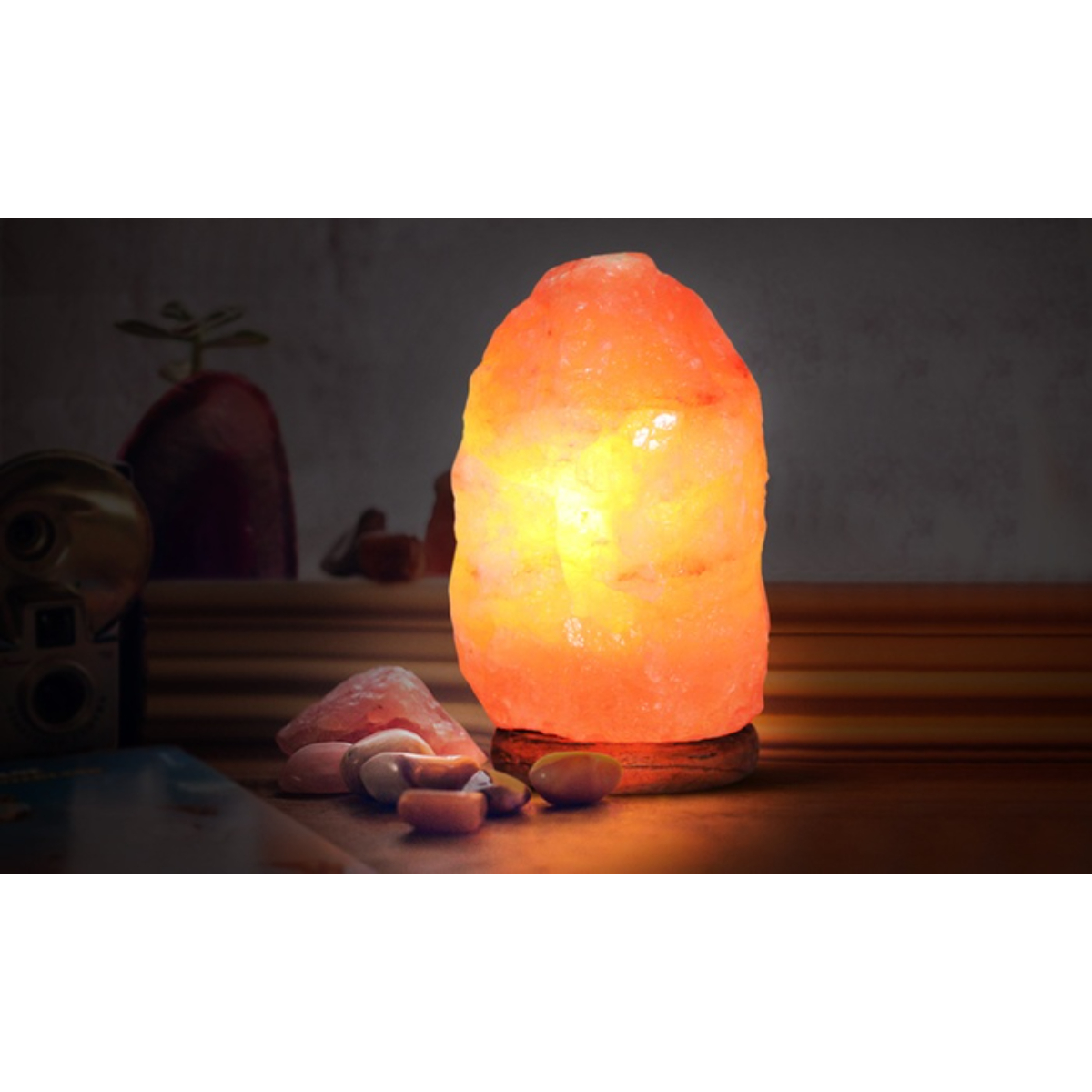 Una lámpara de sal naranja brillante sobre una base de madera, rodeada de rocas y un fondo oscuro.
