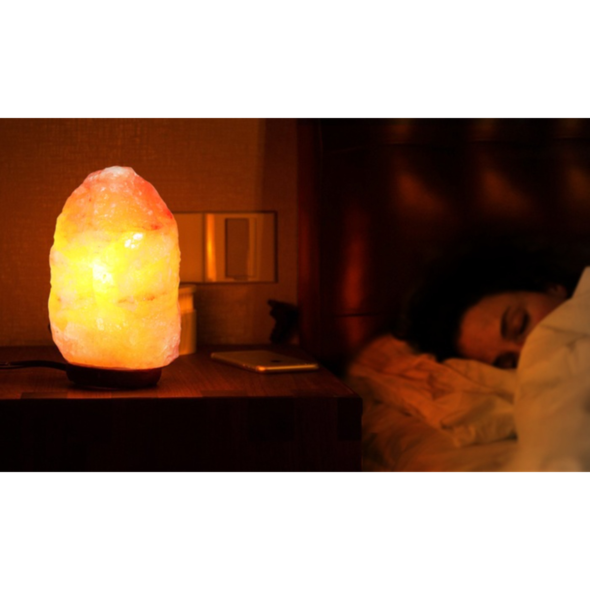 Lámpara de sal brillante en una mesita de noche junto a una persona durmiendo en la cama.