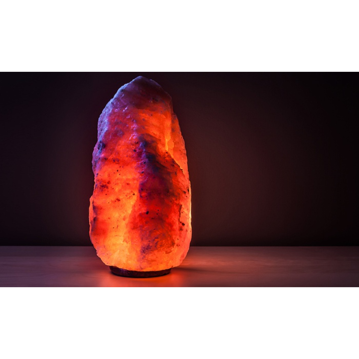 Lámpara de sal brillante sobre una superficie de madera, con un fondo oscuro.