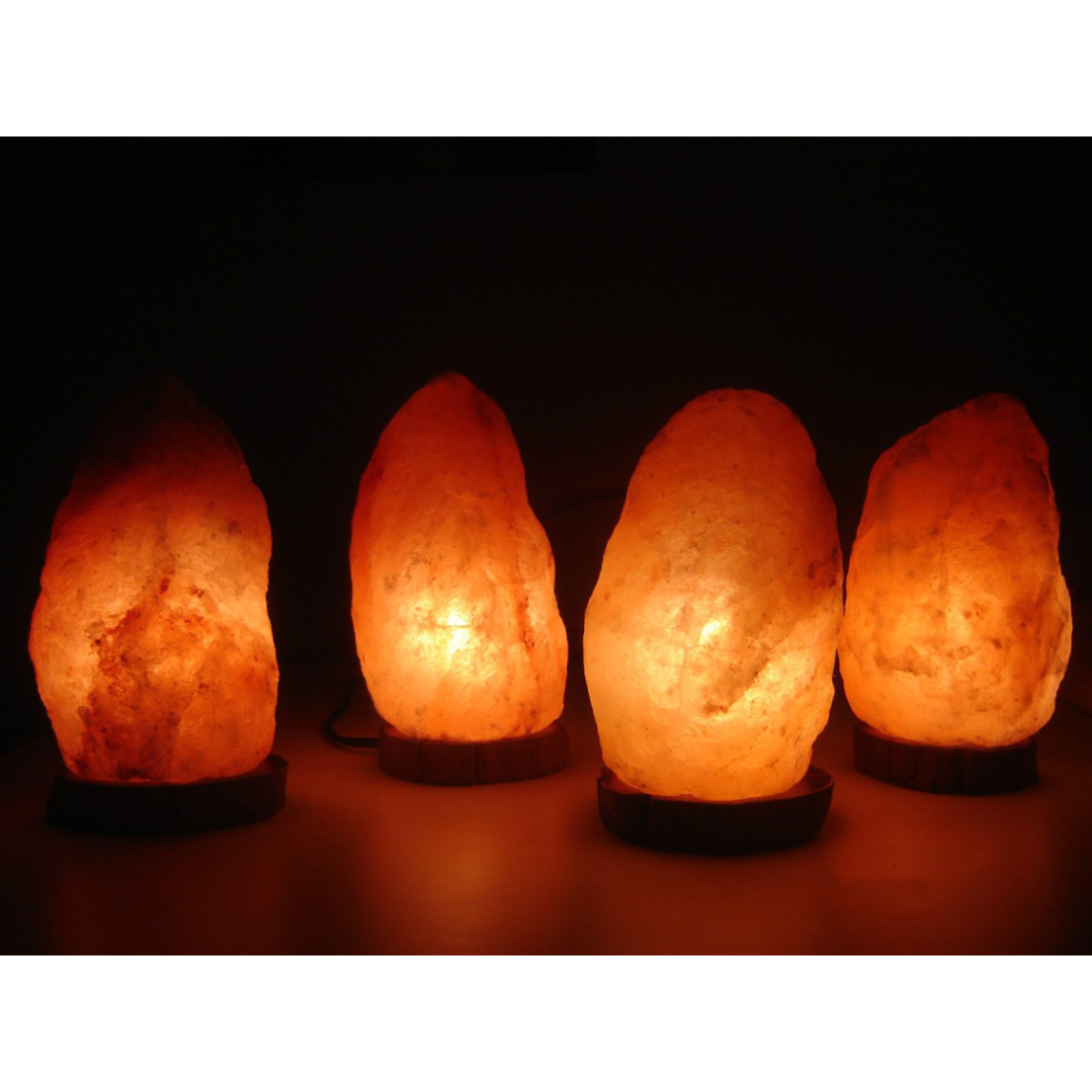 Cuatro lámparas de sal brillantes sobre bases de madera, alineadas.
