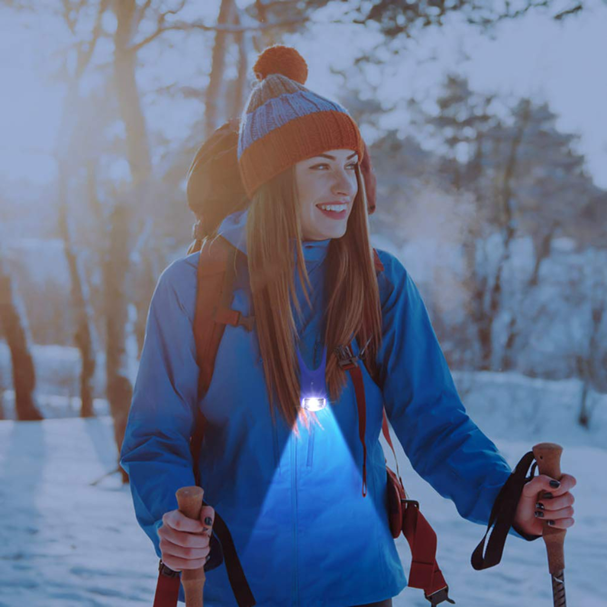 Una mujer con chaqueta azul y un hombre caminan en la nieve, ambos con luces en el cuello.